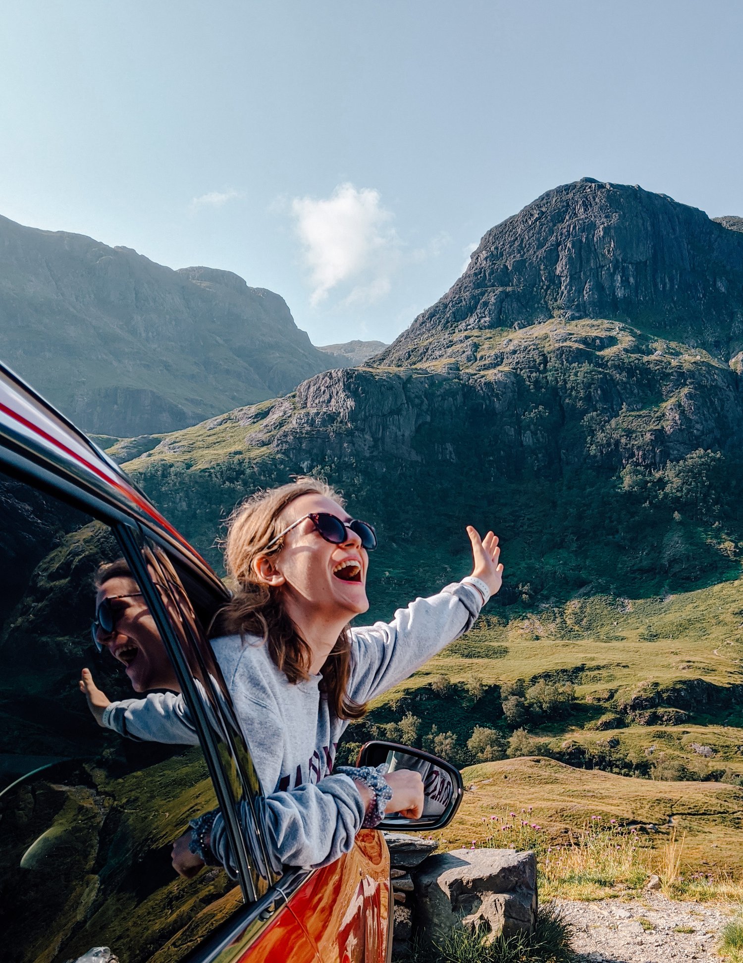Scotland road trip - a girl leaning out a car window with mountains behind her
