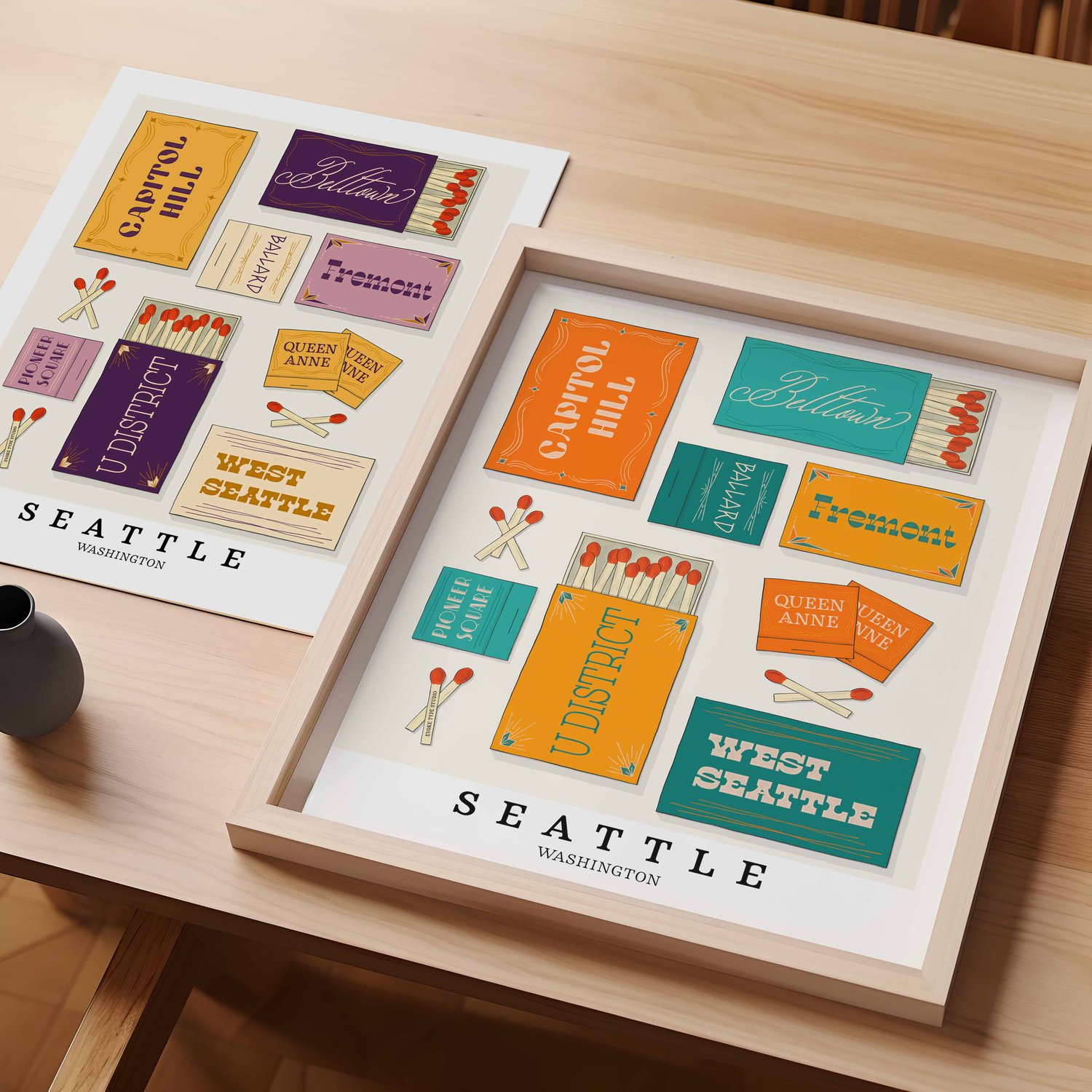 A table with an unframed artwork of Seattle matchbox art and a framed artwork of Seattle matchbox art