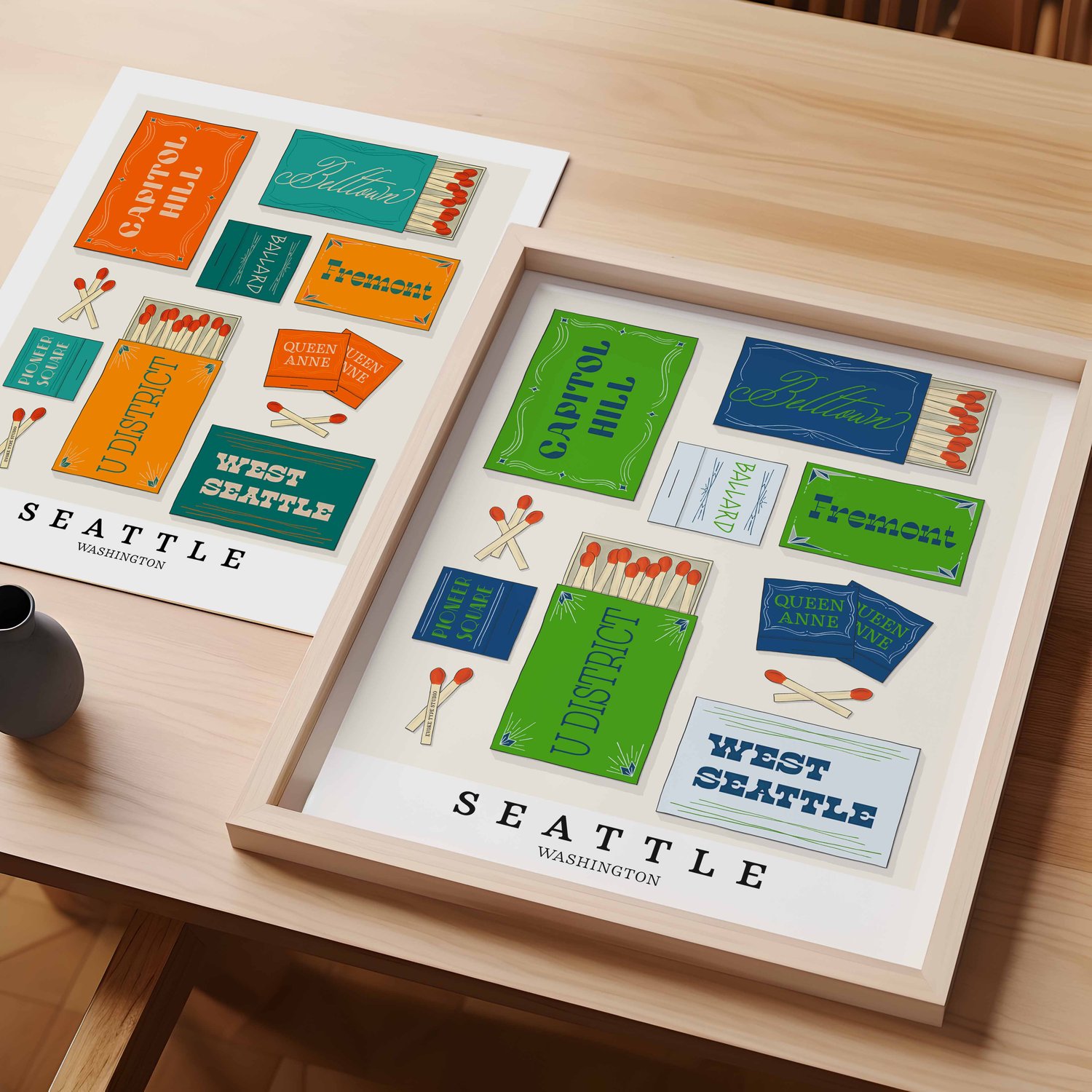 A table with an unframed artwork of Seattle matchbox art and a framed artwork of Seattle matchbox art