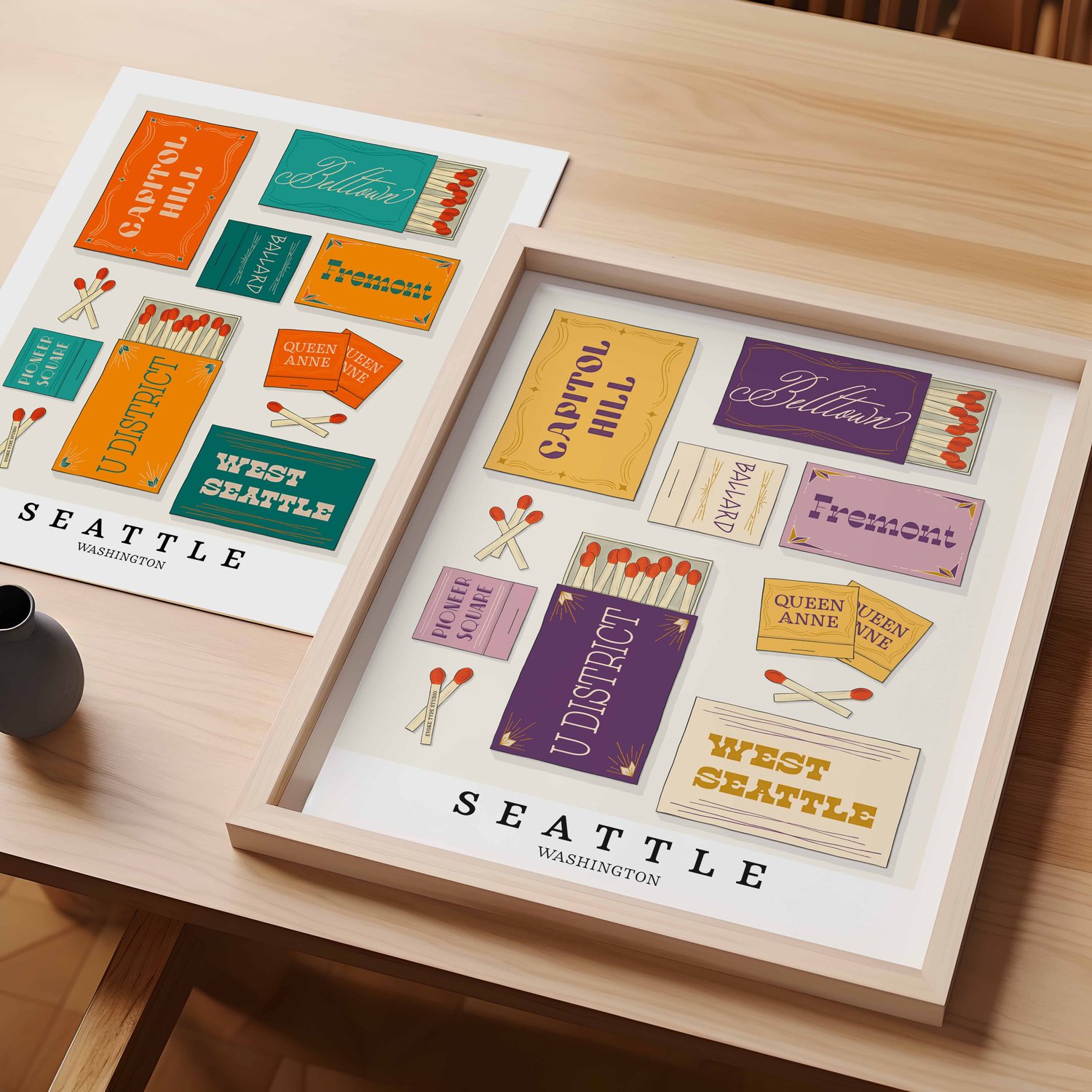 A table with an unframed artwork of Seattle matchbox art and a framed artwork of Seattle matchbox art
