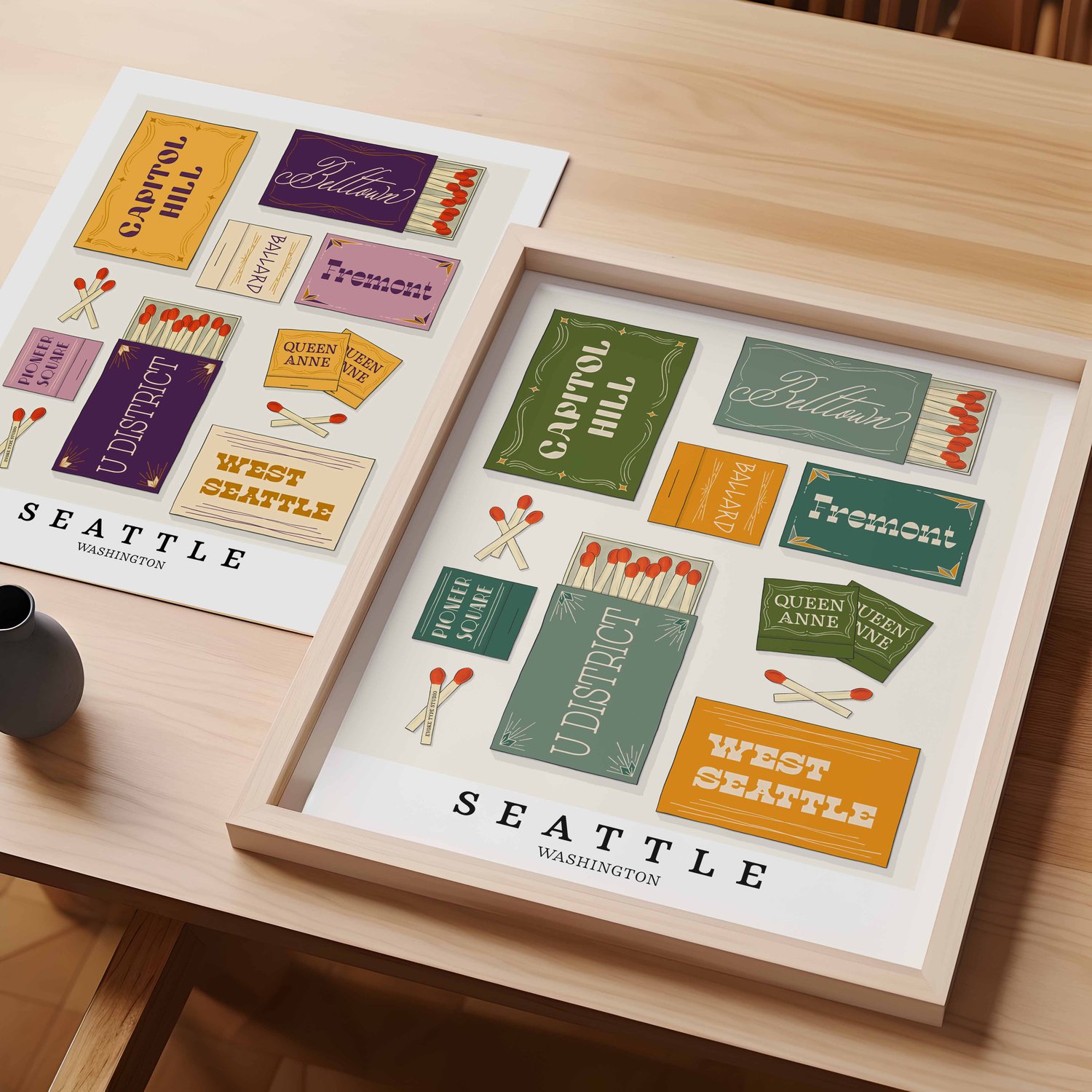 A table with an unframed artwork of Seattle matchbox art and a framed artwork of Seattle matchbox art