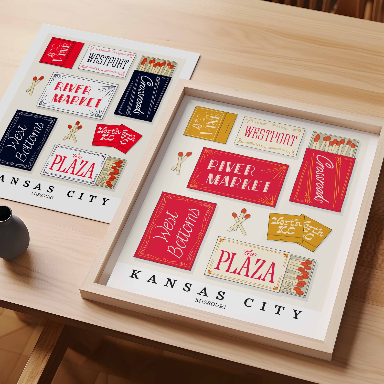 A table with an unframed artwork of Kansas City matchbox art and a framed artwork of Kansas City matchbox art