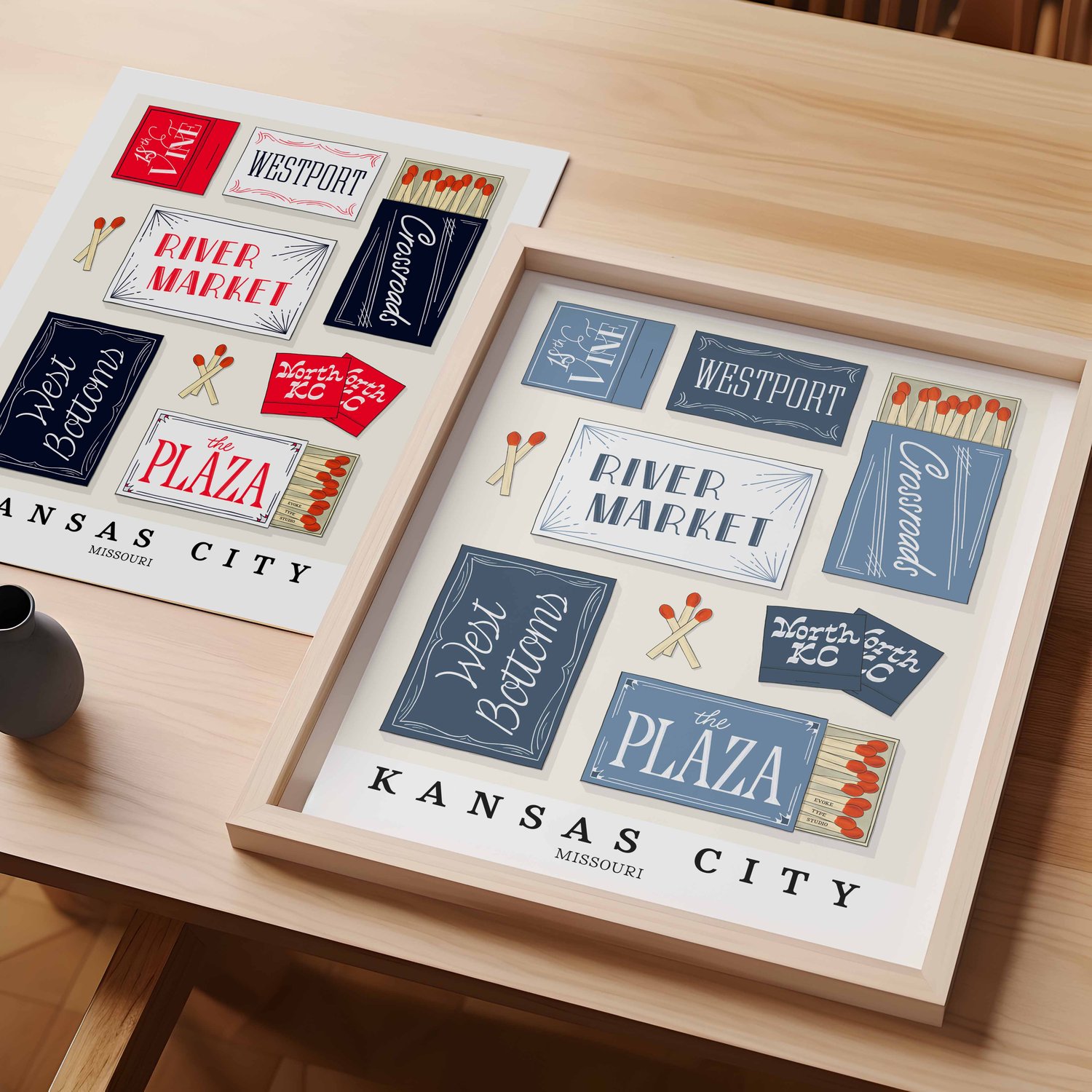 A table with an unframed artwork of Kansas City matchbox art and a framed artwork of Kansas City matchbox art