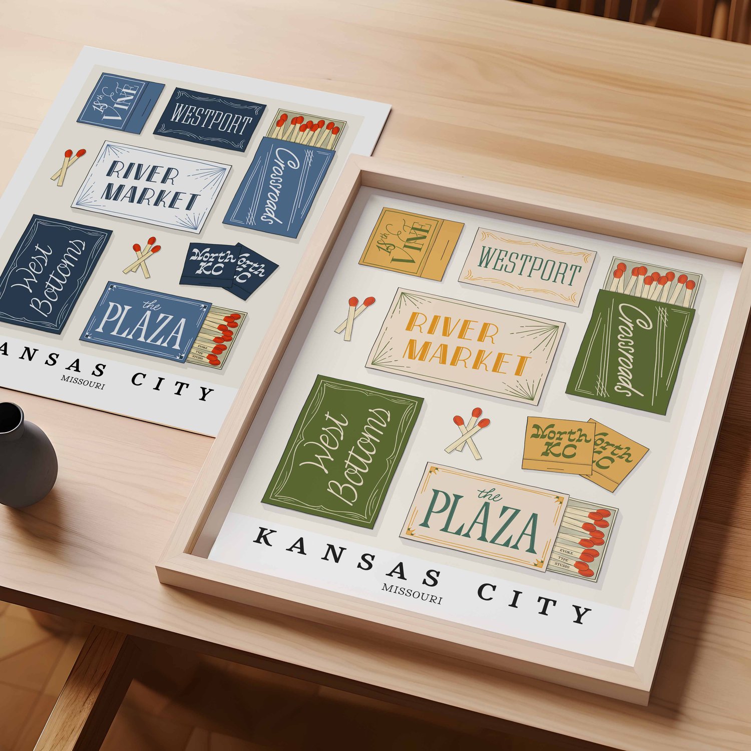 A table with an unframed artwork of Kansas City matchbox art and a framed artwork of Kansas City matchbox art