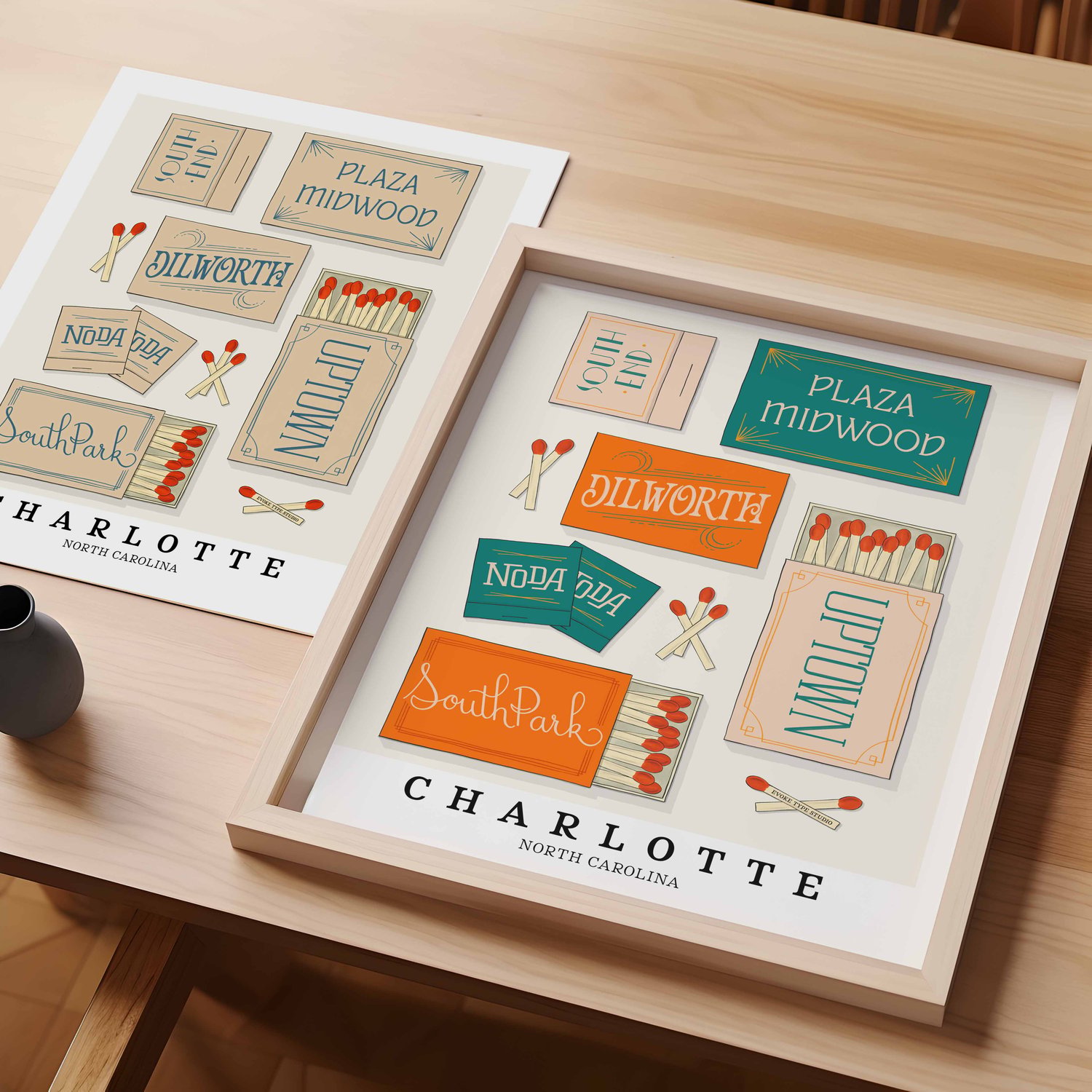 A table with an unframed artwork of Charlotte matchbox art and a framed artwork of Charlotte matchbox art