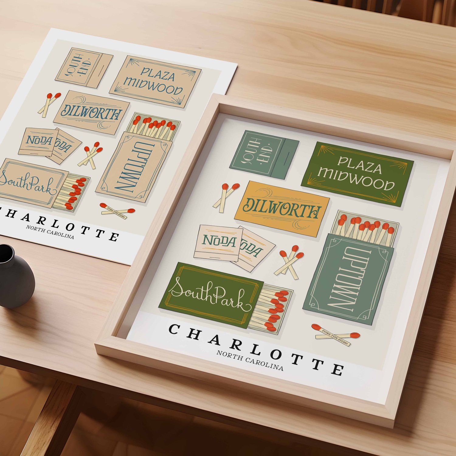 A table with an unframed artwork of Charlotte matchbox art and a framed artwork of Charlotte matchbox art