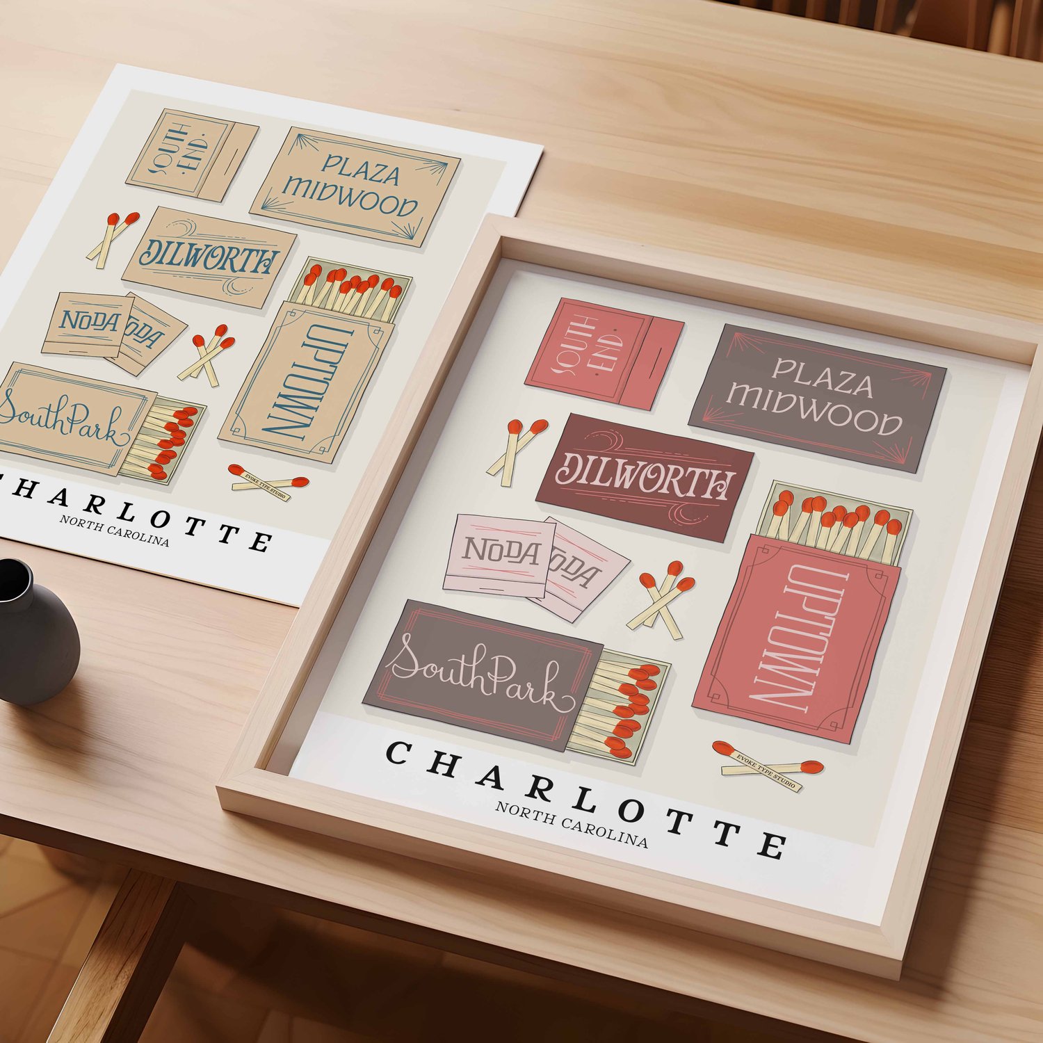 A table with an unframed artwork of Charlotte matchbox art and a framed artwork of Charlotte matchbox art