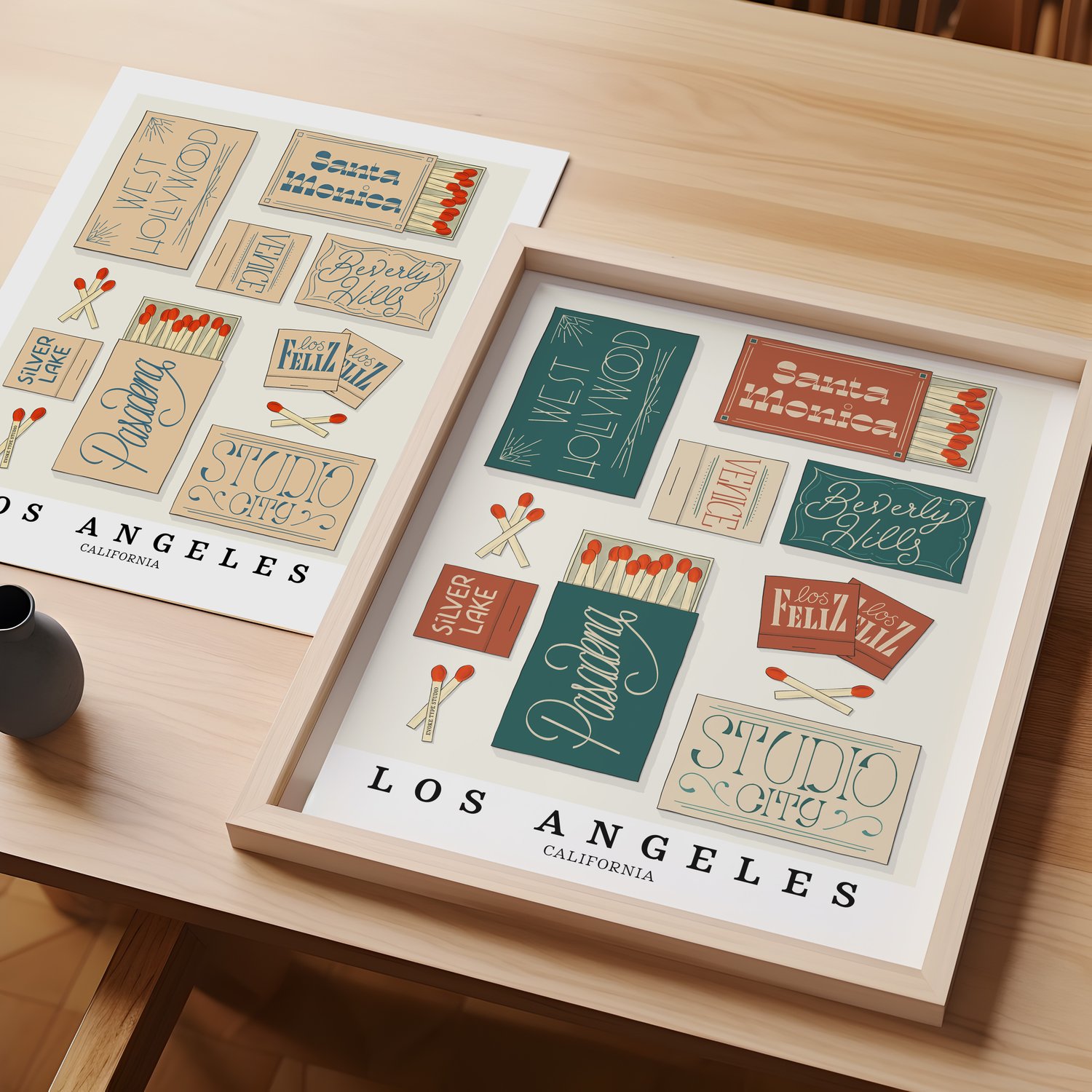 A table with an unframed artwork of Los Angeles matchbox art and a framed artwork of Los Angeles matchbox art