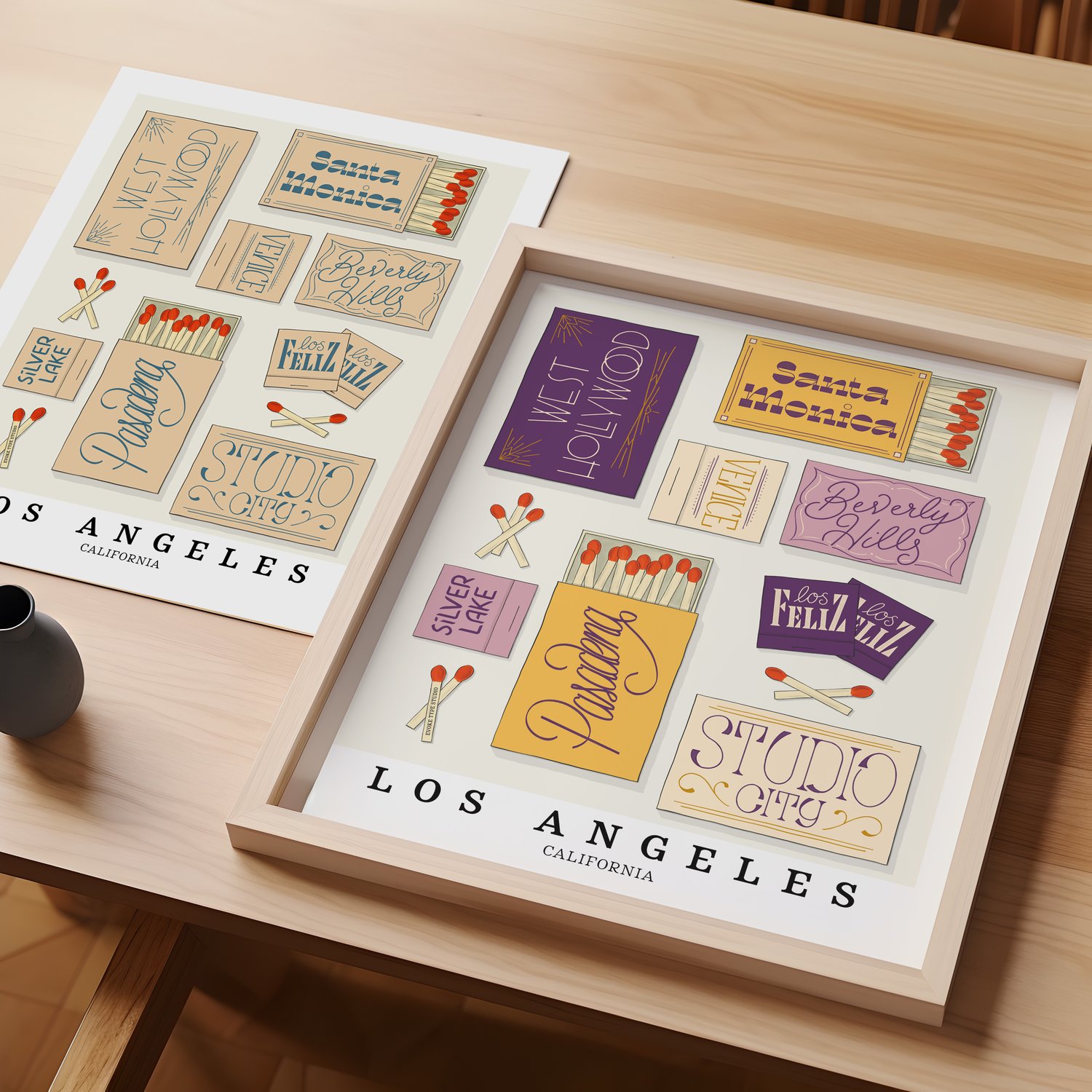 A table with an unframed artwork of Los Angeles matchbox art and a framed artwork of Los Angeles matchbox art