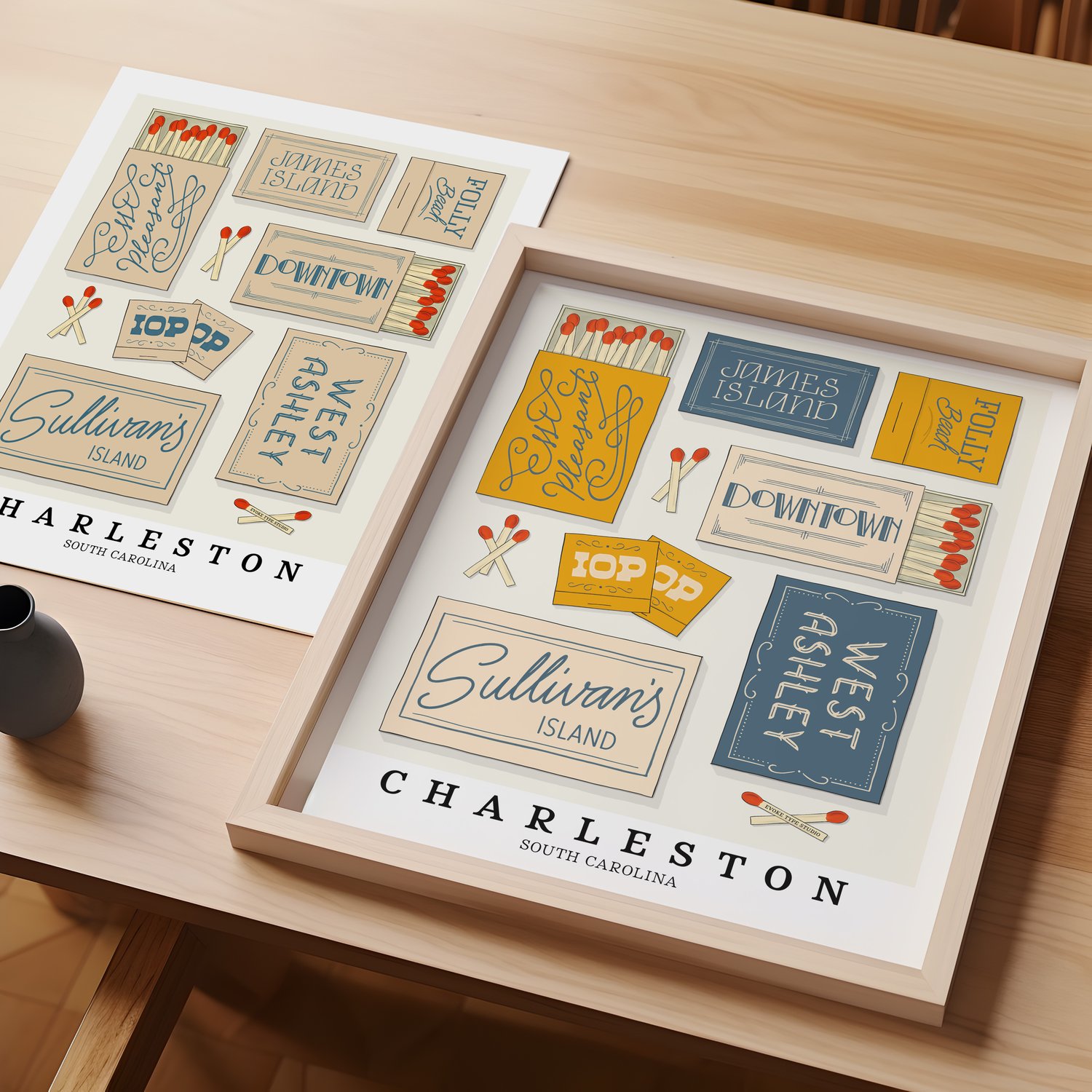 A table with an unframed artwork of Charleston matchbox art and a framed artwork of Charleston matchbox art