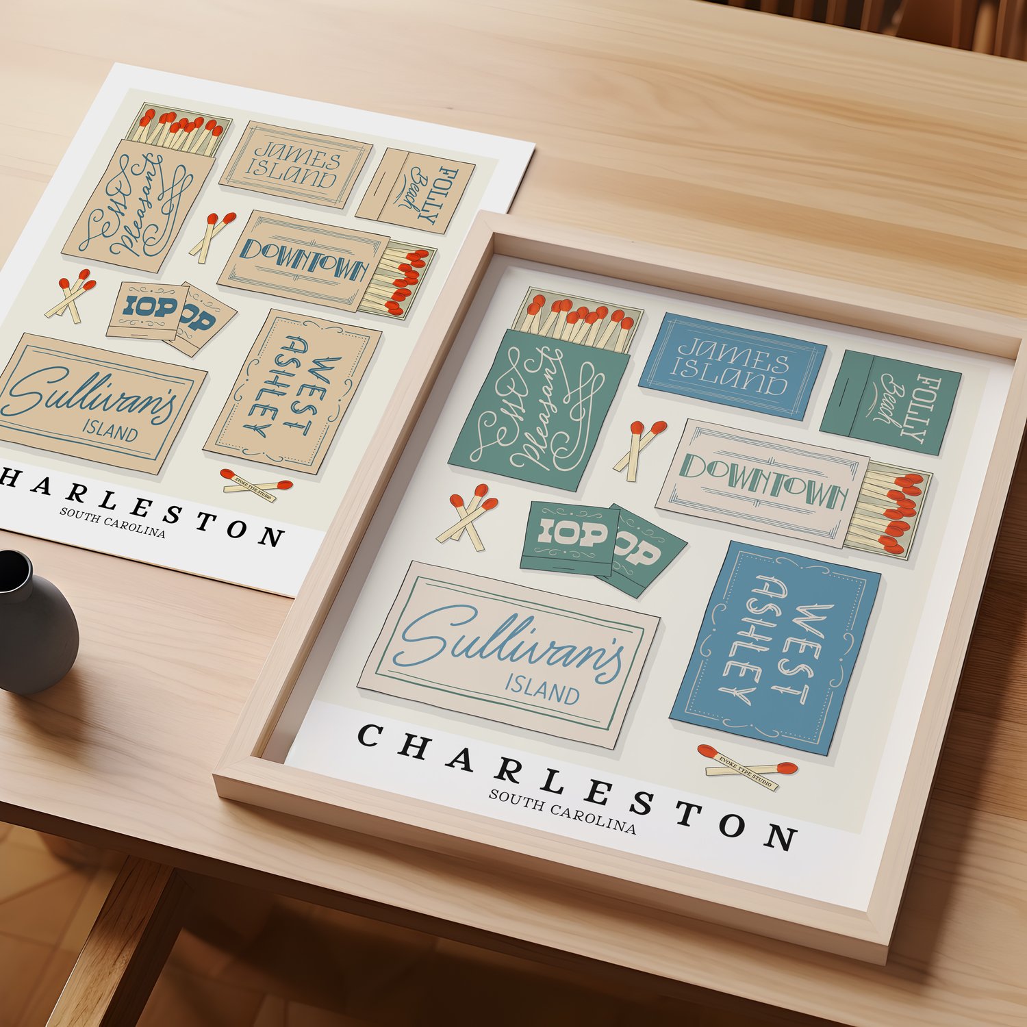 A table with an unframed artwork of Charleston matchbox art and a framed artwork of Charleston matchbox art