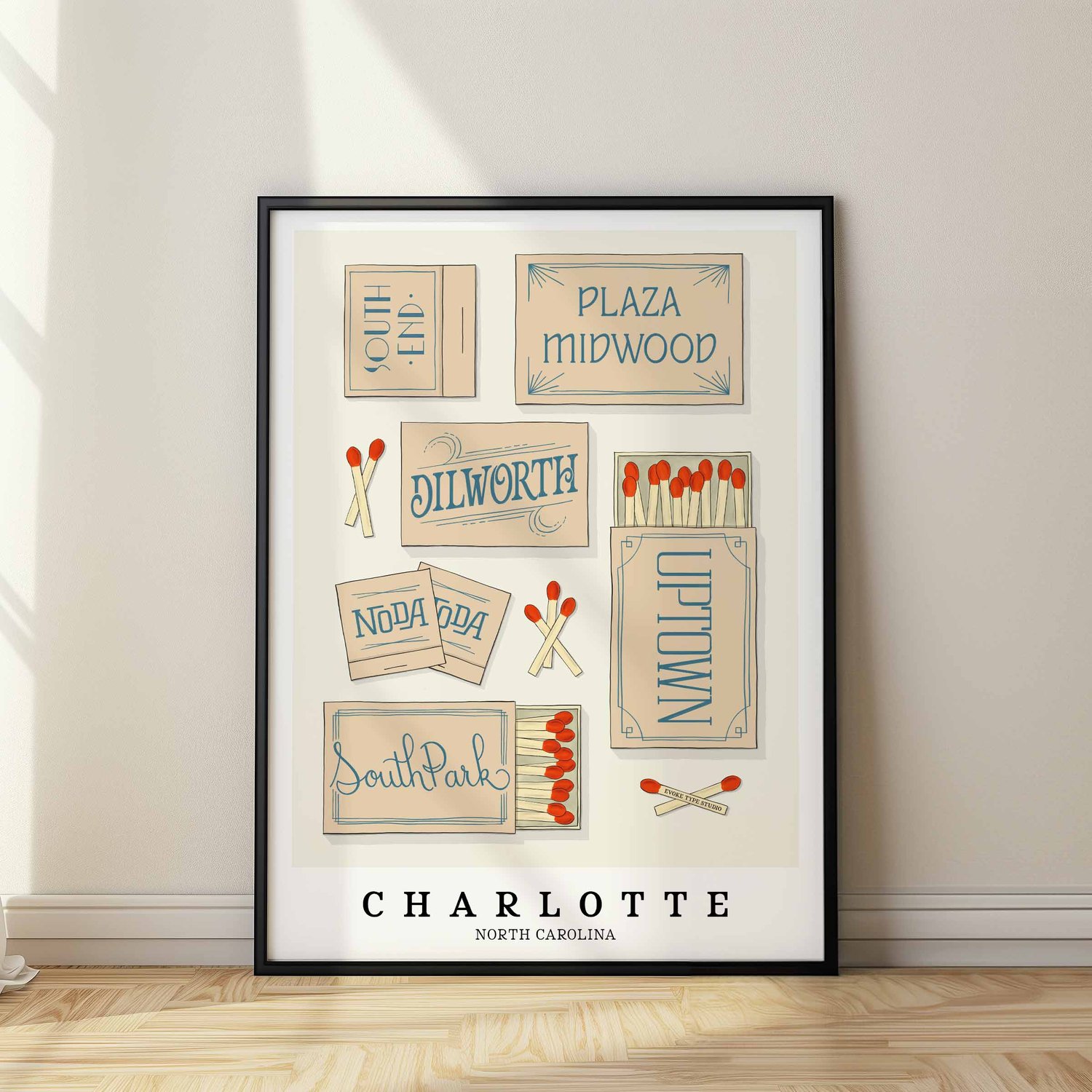 A framed picture of Charlotte, North Carolina neighborhoods drawn in various lettering styles on matchboxes. Artwork has a beige and blue color scheme