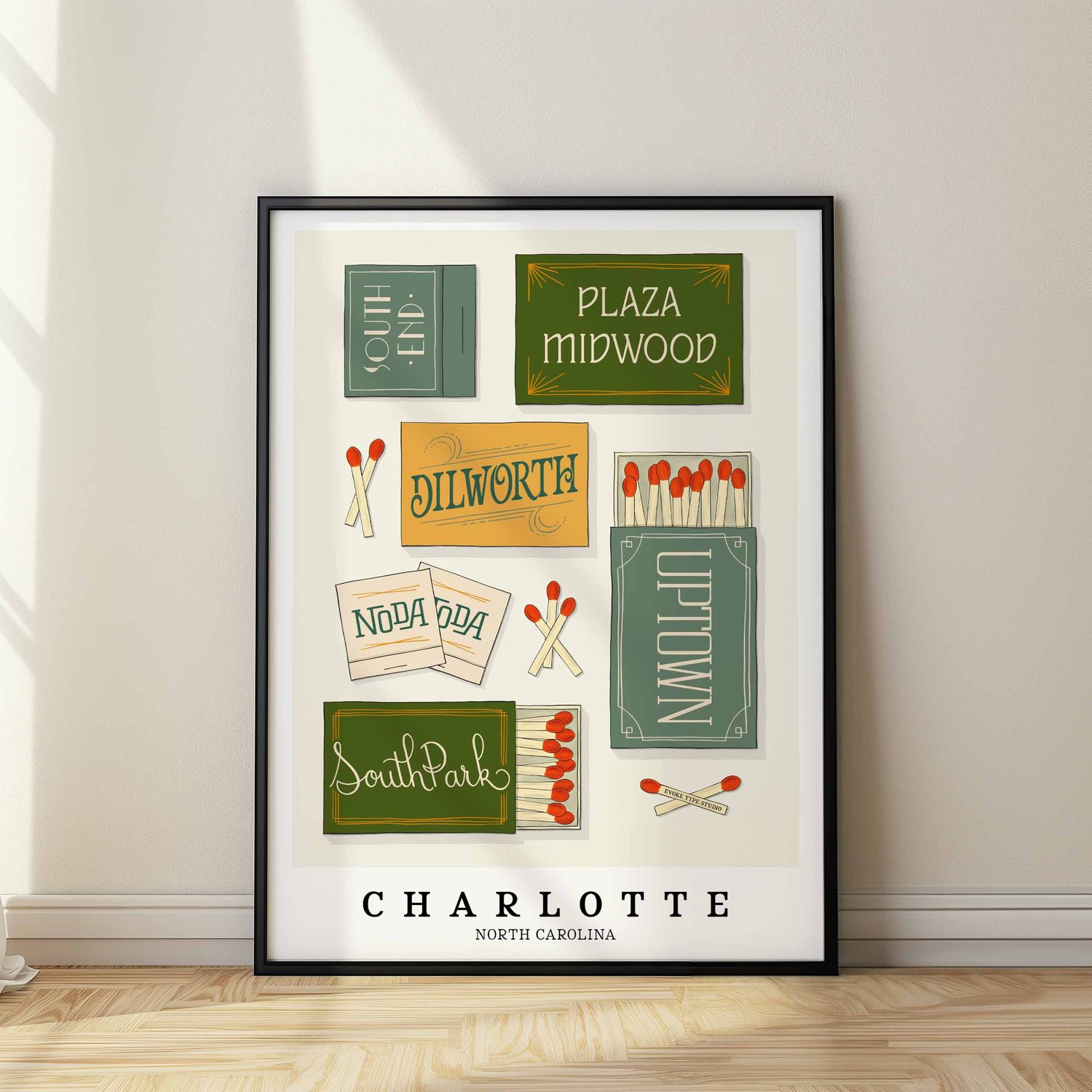 A framed picture of Charlotte, North Carolina neighborhoods drawn in various lettering styles on matchboxes. Artwork has a blue, green and yellow color scheme