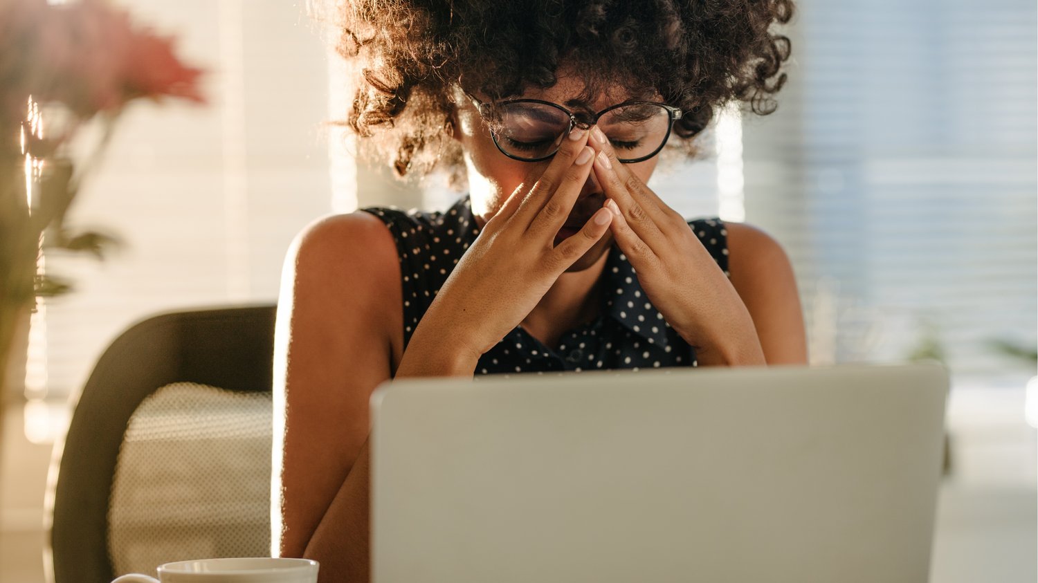 Stressed female health coach sitting at her laptop with hands on face, experiencing self-doubt—representing imposter syndrome and the emotional challenges faced by new wellness coaches.