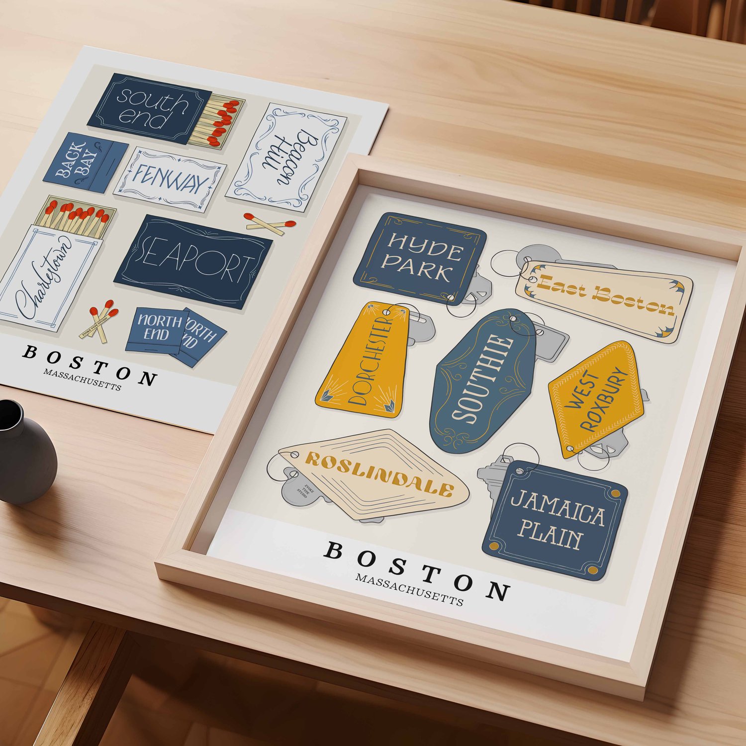 A table with an unframed artwork of Boston matchbox art and a framed artwork of Boston key fob art