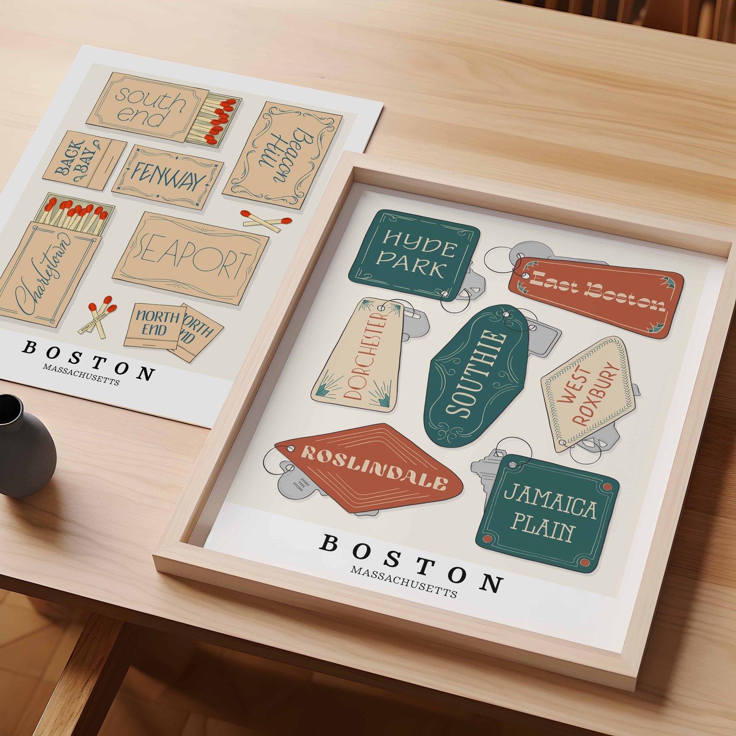 A table with an unframed artwork of Boston matchbox art and a framed artwork of Boston key fob art