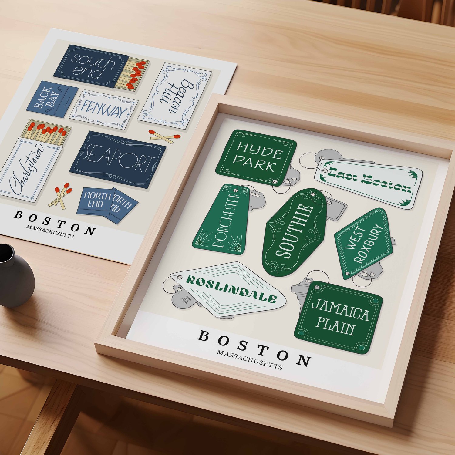 A table with an unframed artwork of Boston matchbox art and a framed artwork of Boston key fob art