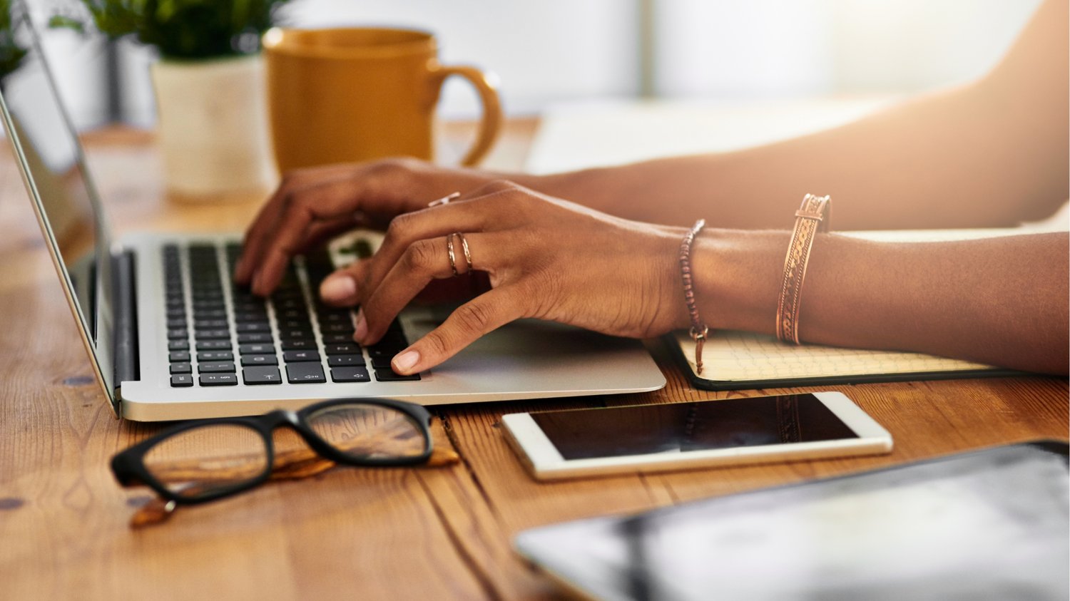 Close-up of a health coach typing on a laptop at a wooden desk with a notebook and smartphone—illustrating email marketing for health coaches and the importance of building an email list to grow a coaching business.
