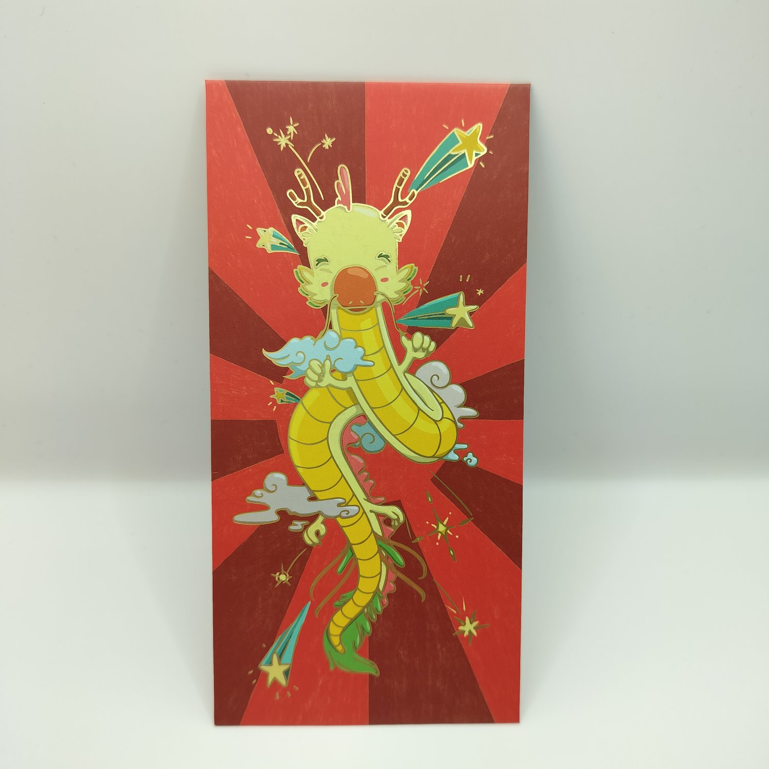 Red hongbao with radiating sunburst pattern featuring a colorful cartoon dragon in yellow and green with clouds, stars, and decorative elements in an animated, festive style.