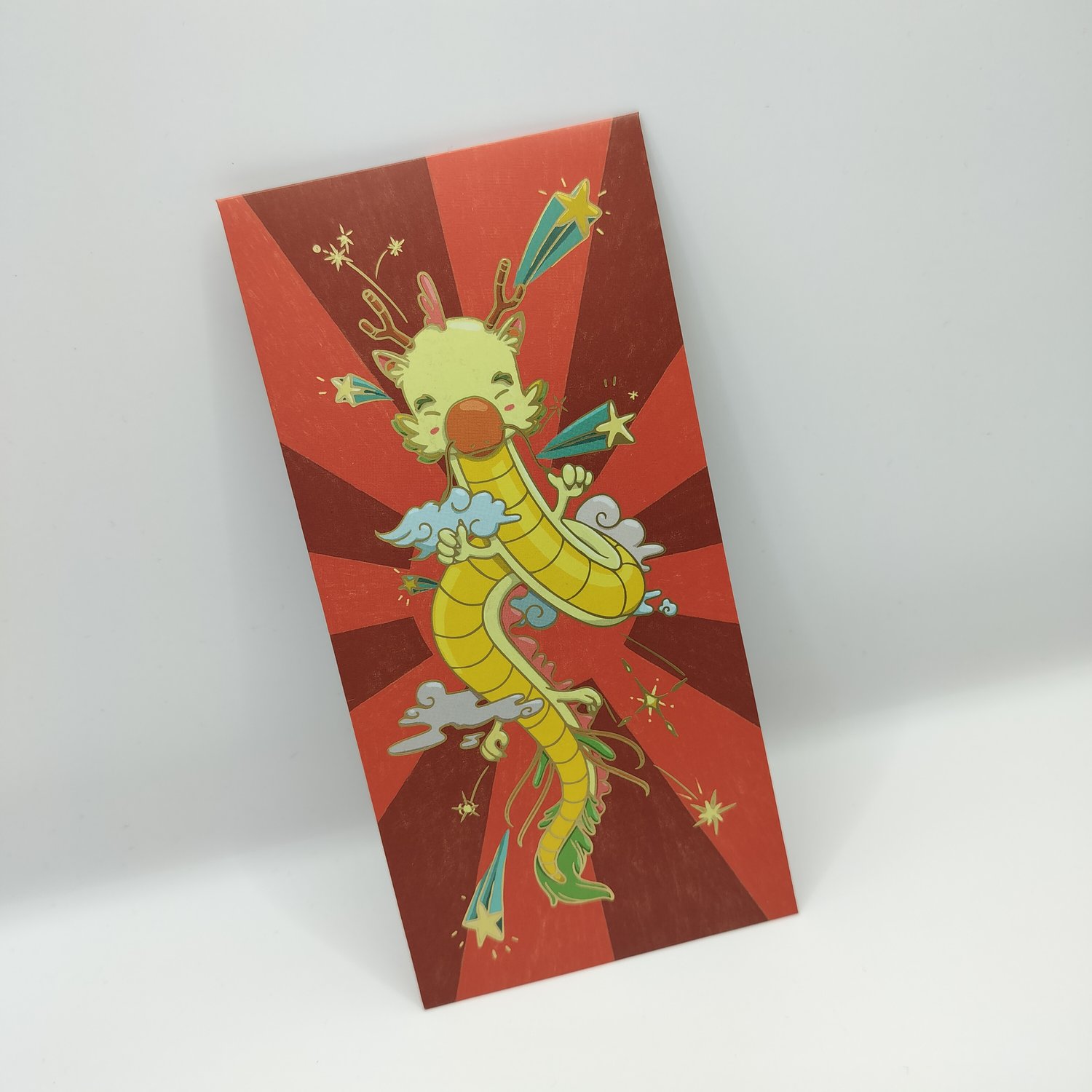 Red hongbao with radiating sunburst pattern featuring a colorful cartoon dragon in yellow and green with clouds, stars, and decorative elements in an animated, festive style.