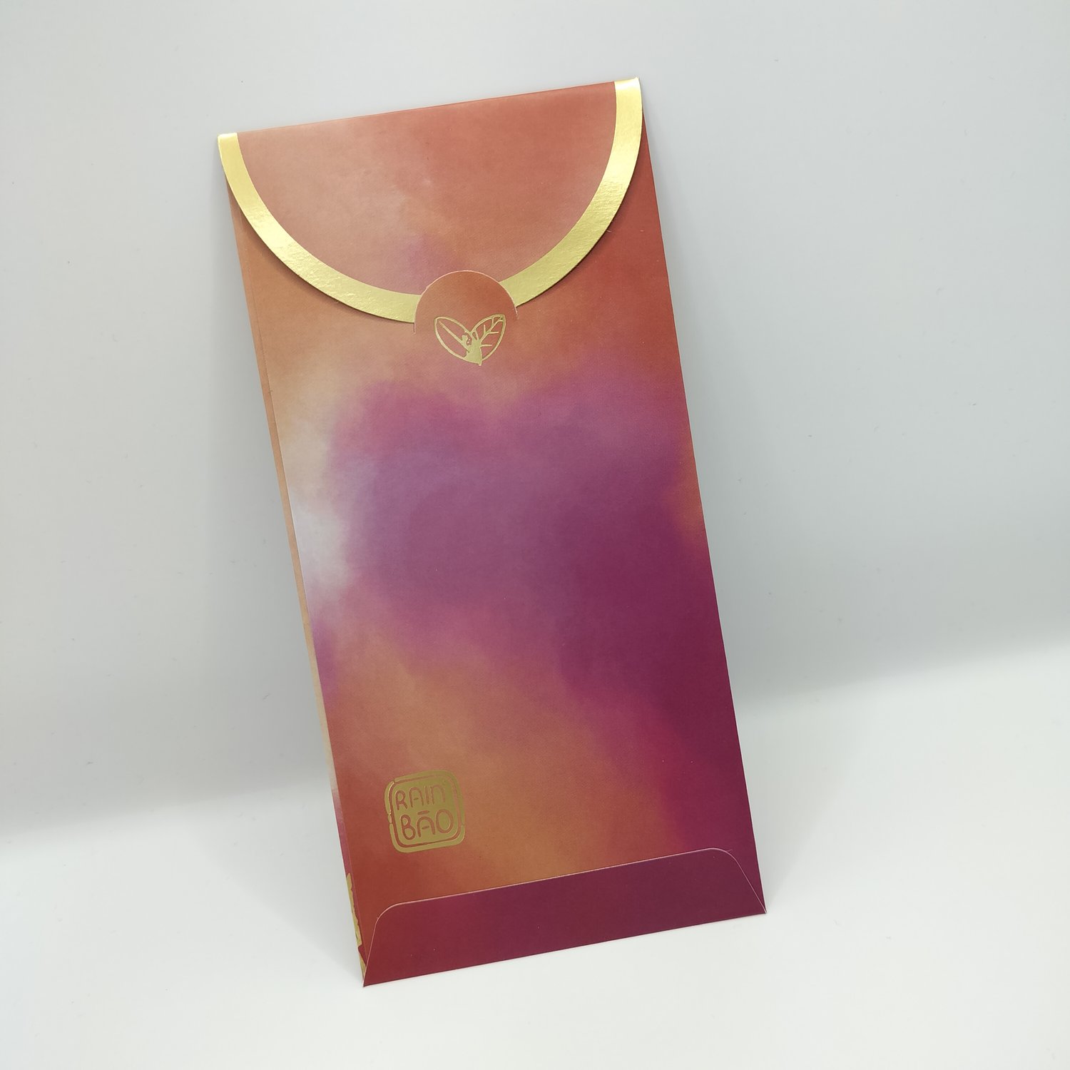 The back of a red, orange and pink gradient envelope with gold trim and small botanical motifs and a logo in the bottom left corner.