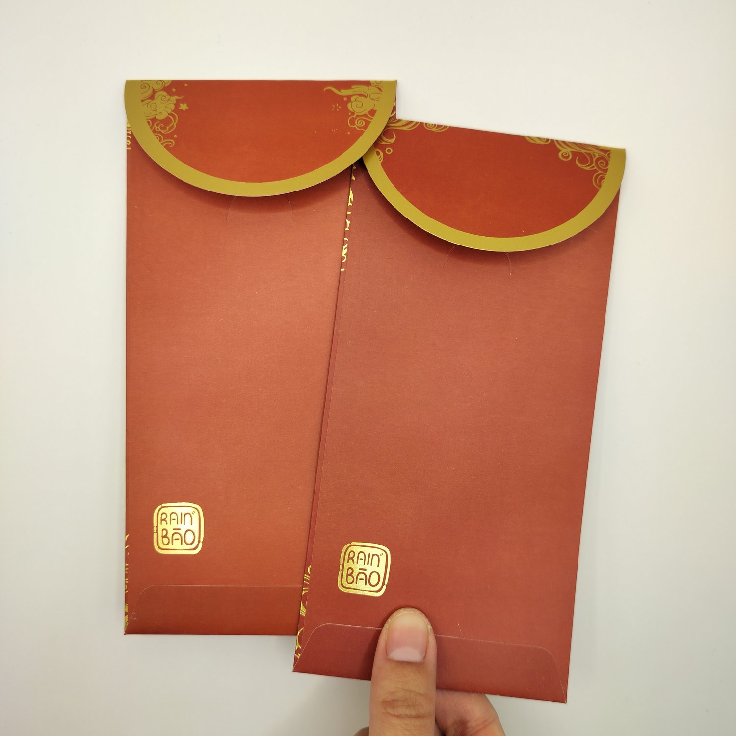 The backs of two red hongbaos with gold foil trim on the closing flaps.