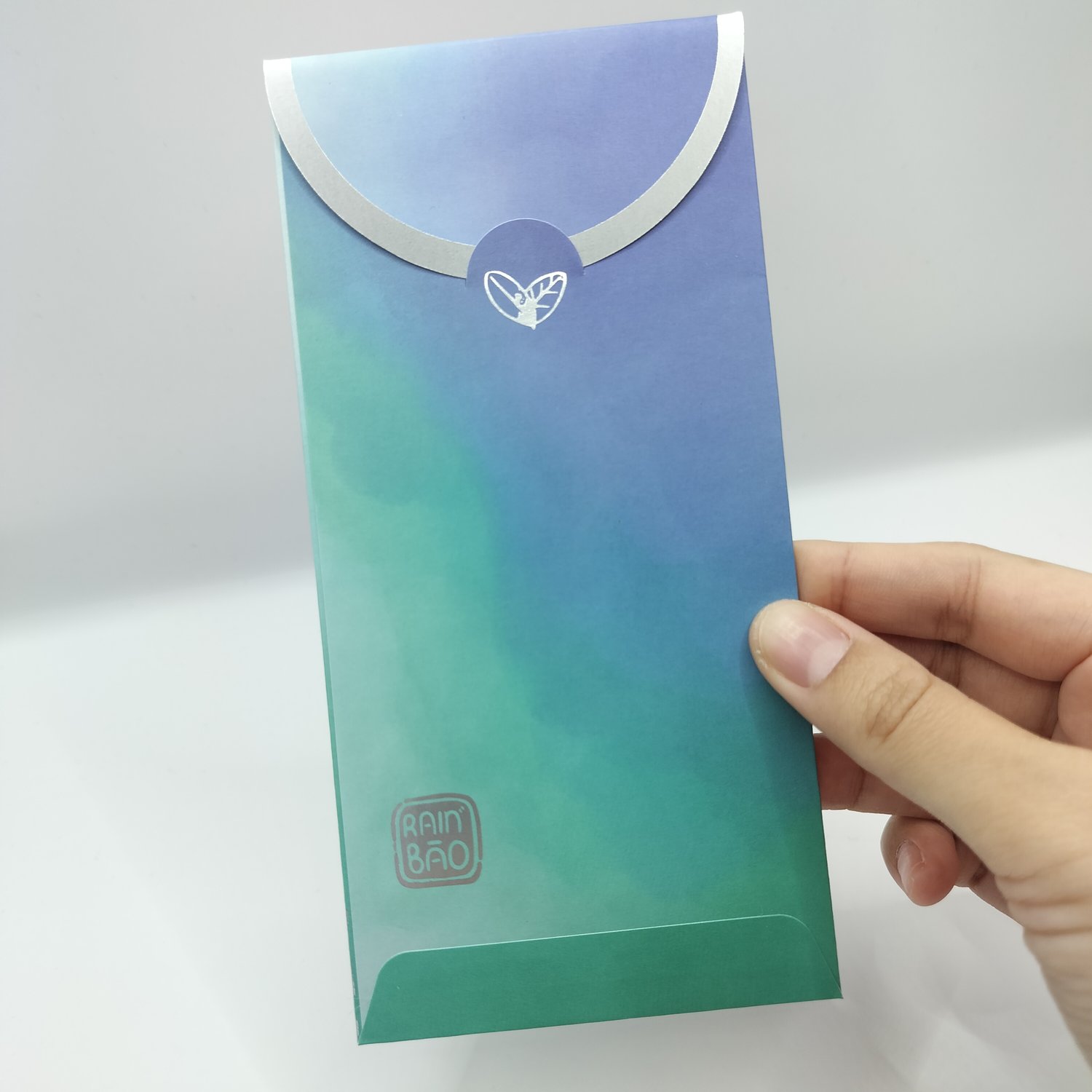 The back of a blue-to-teal gradient envelope with silver botanical foil illustrations.