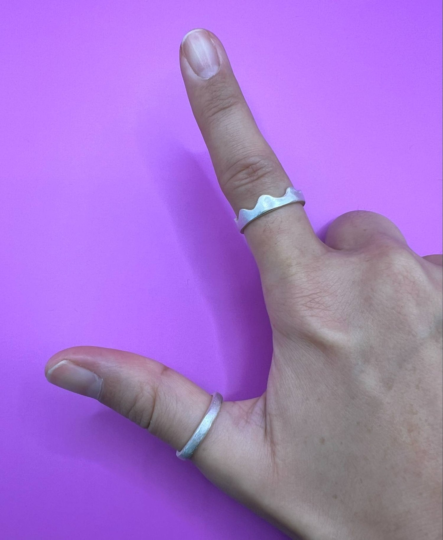 A hand wearing two silver rings. One has a wavy, scalloped edge and the other is a plain band.