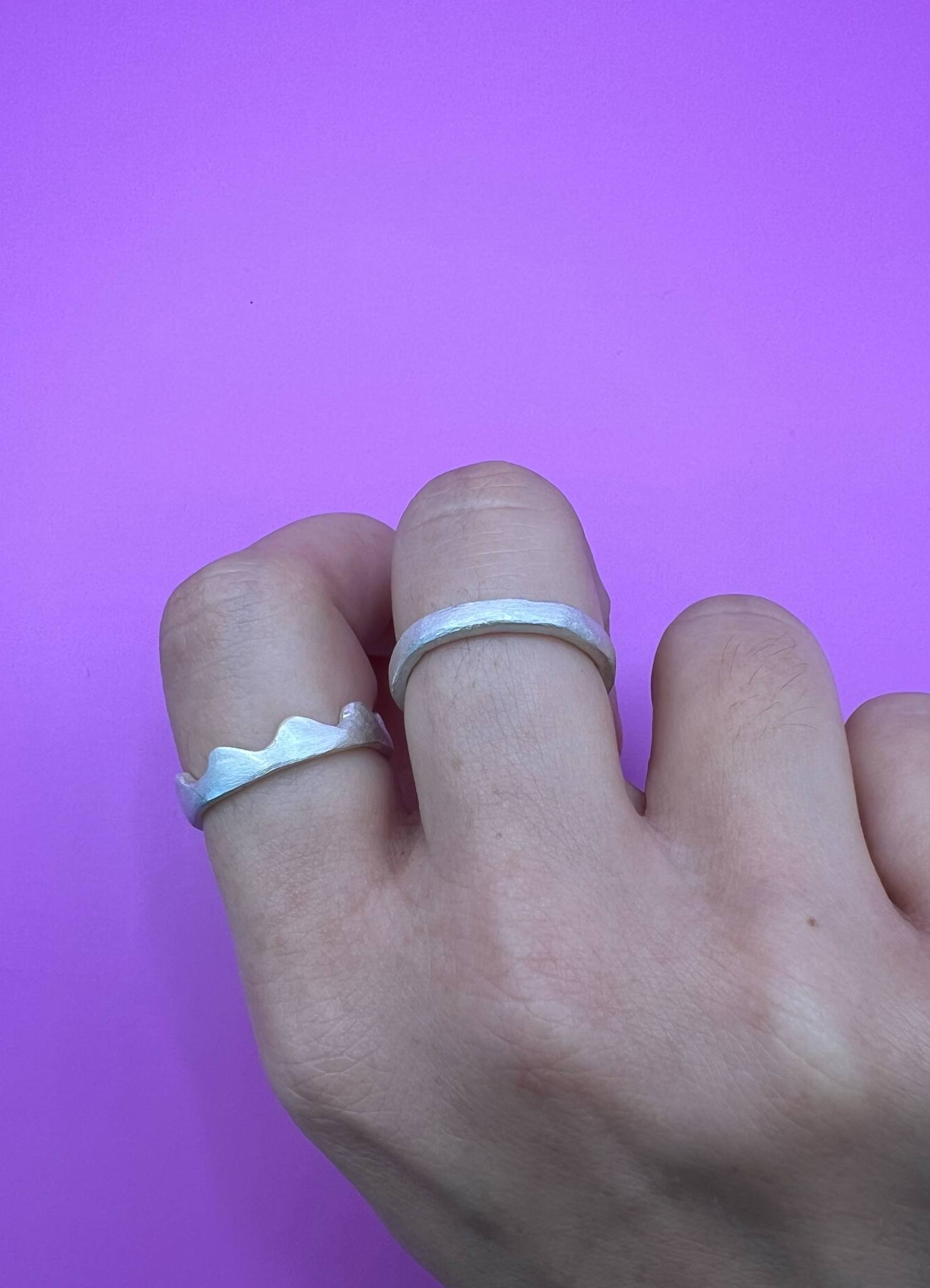A hand wearing two silver rings. One has a wavy, scalloped edge and the other is a plain band.