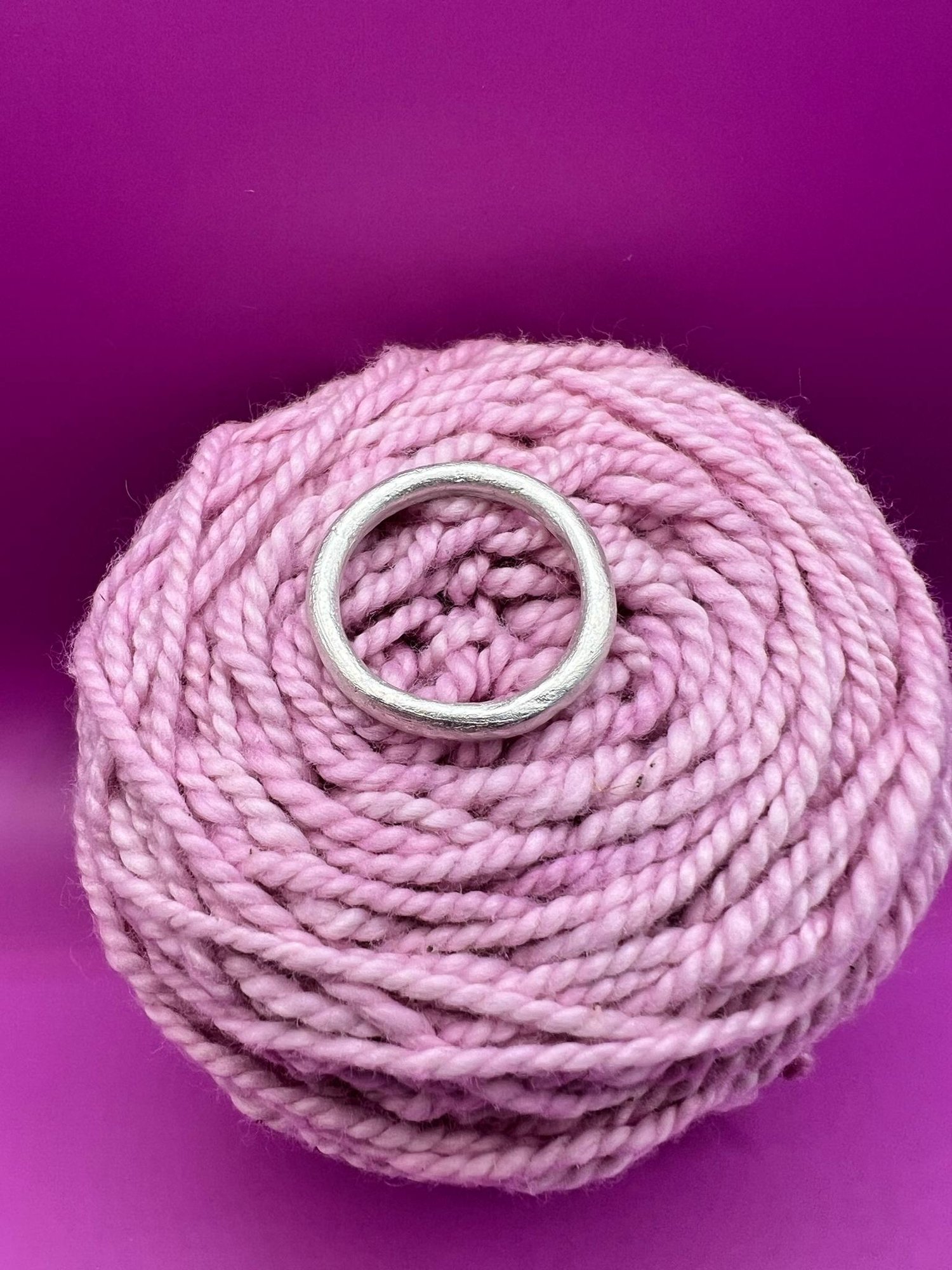 Side profile of a silver band ring with a rounded profile resting on pink yarn.