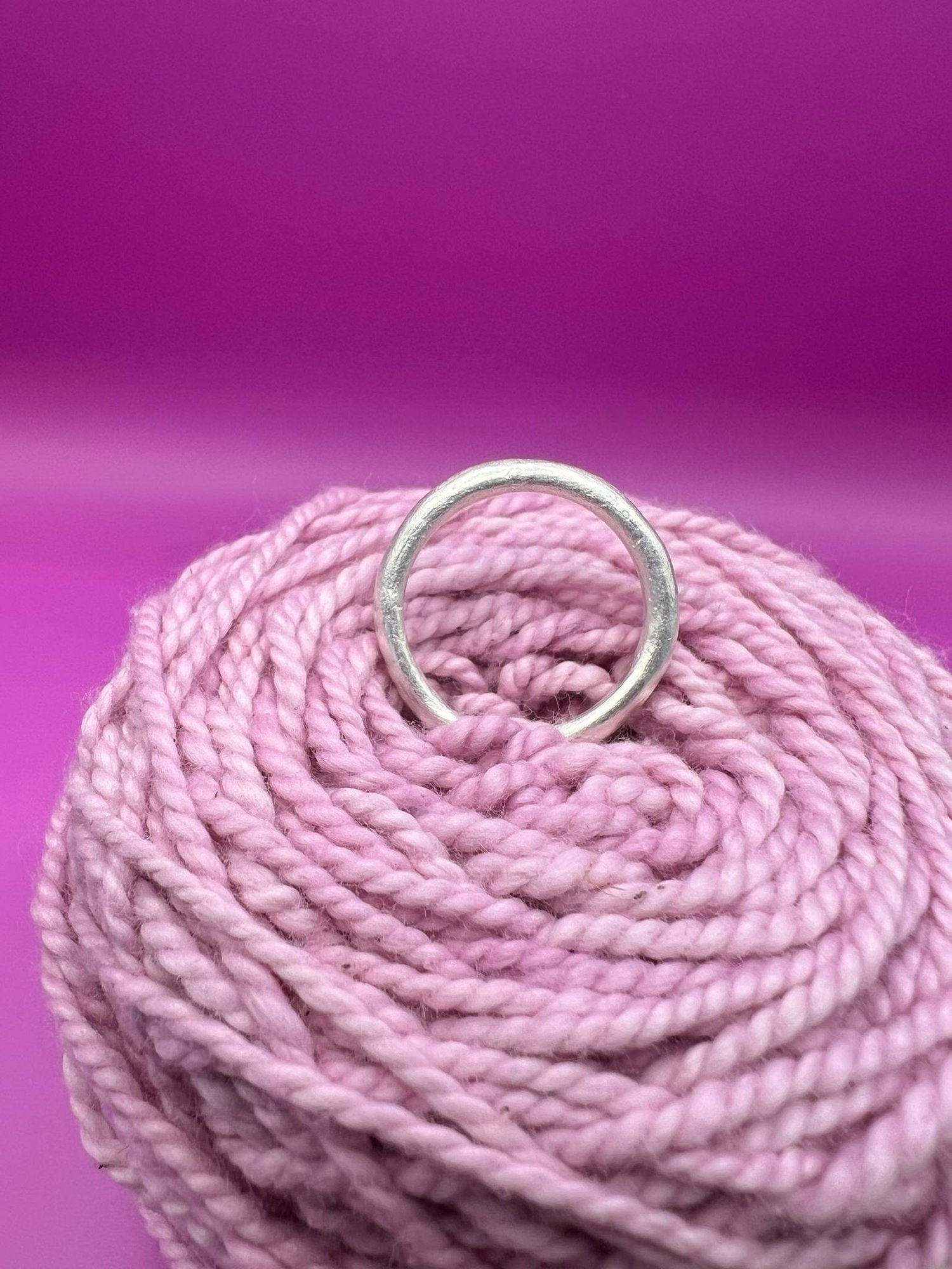 A silver band ring with a rounded profile resting on pink yarn.