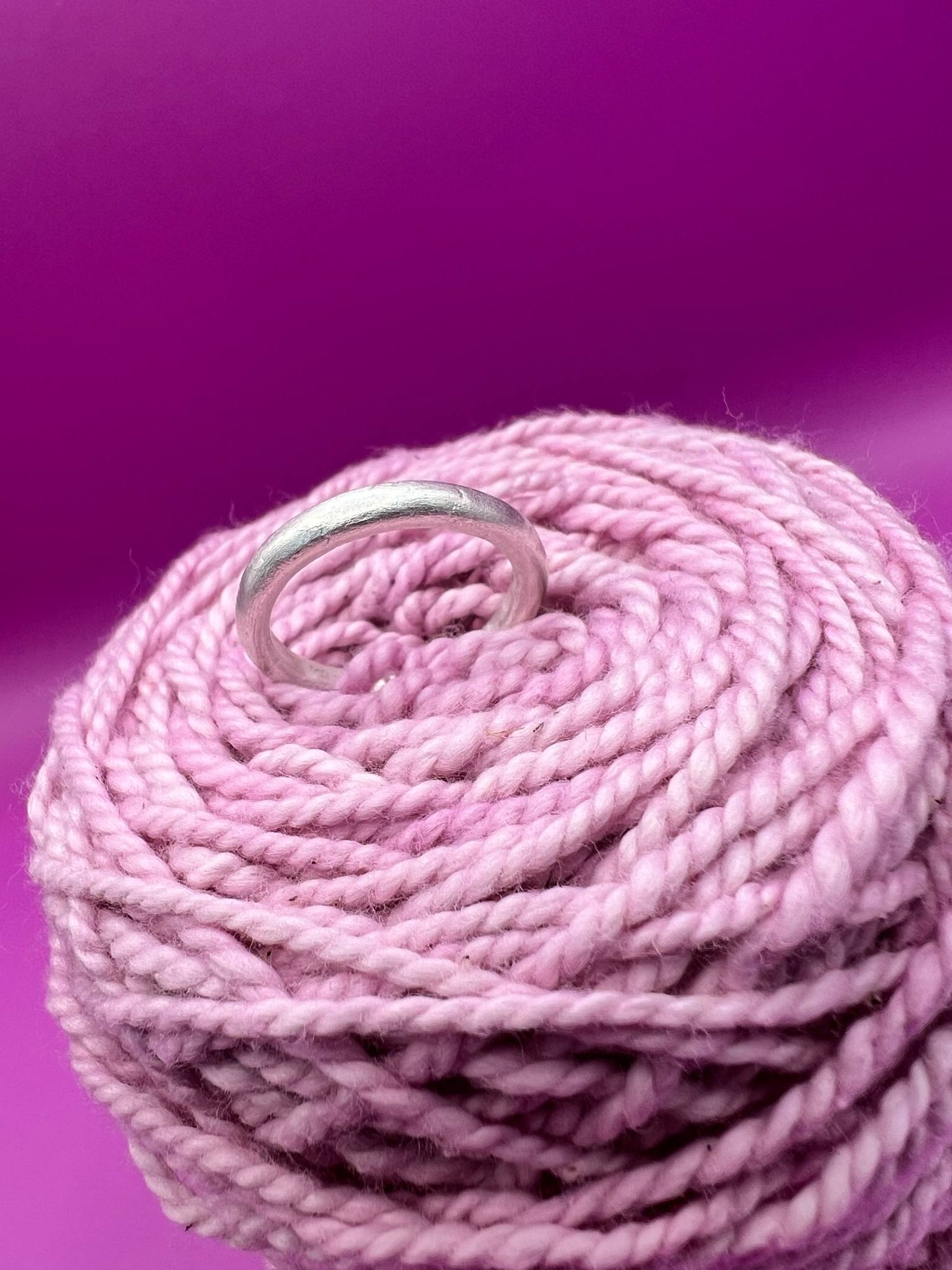 A silver band ring with a rounded profile resting on pink yarn.