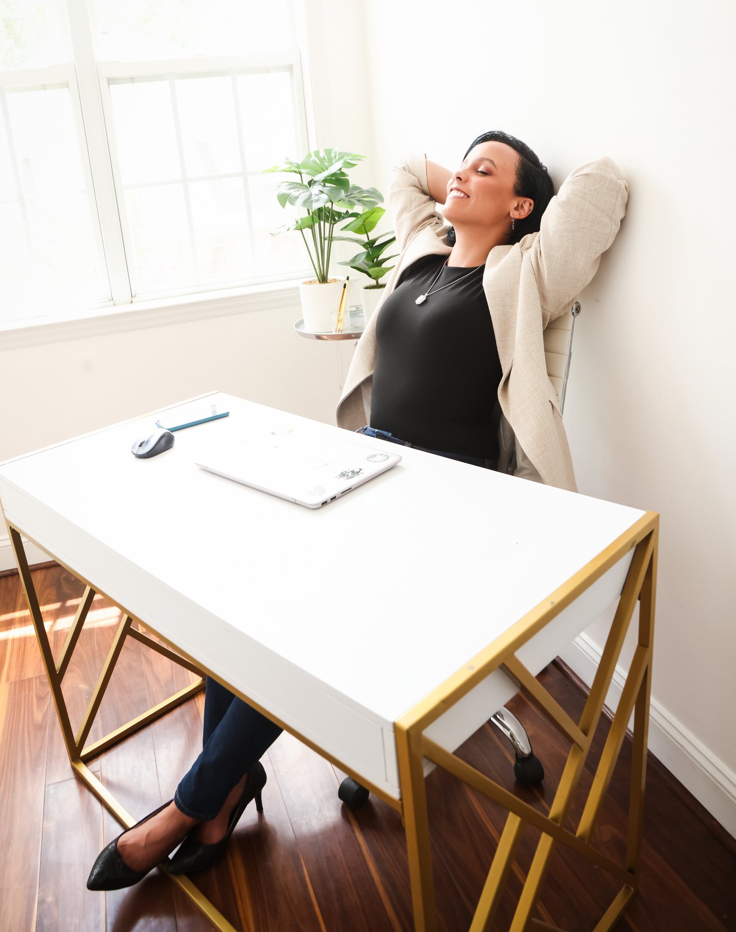 Whitney sits at a desk and leans back, smiling. Image credit: Elizabeth Ashley & Co.