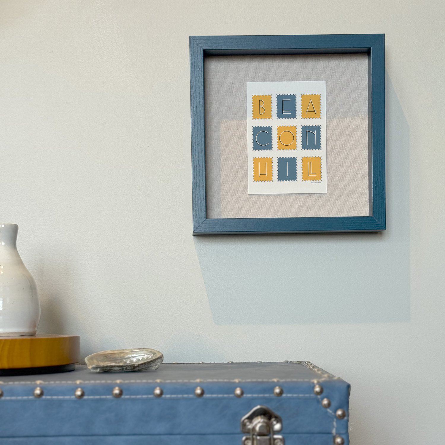A framed notecard in a shadow box hung on the wall with decorative items placed nearby.