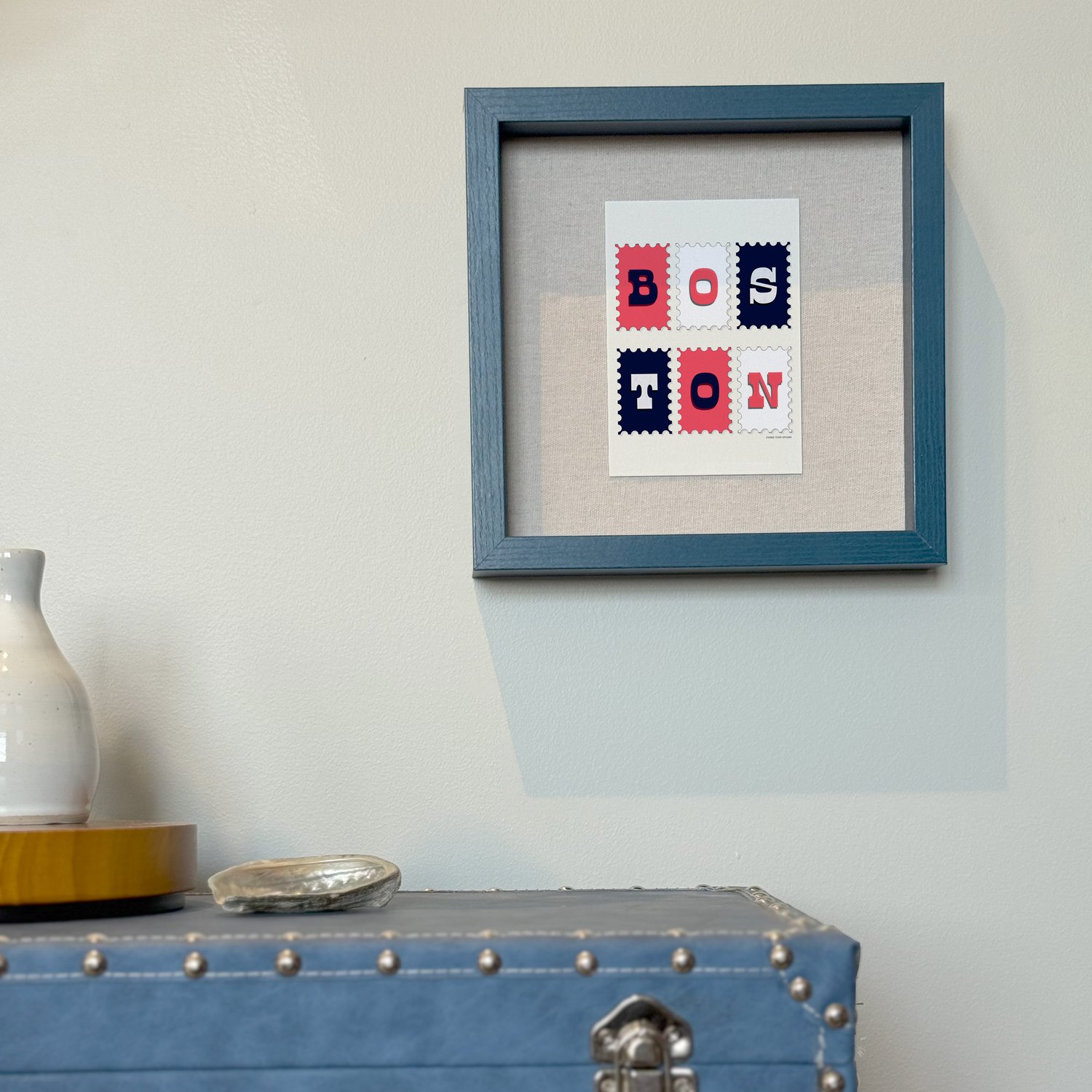 A framed notecard in a shadow box hung on the wall with decorative items placed nearby.