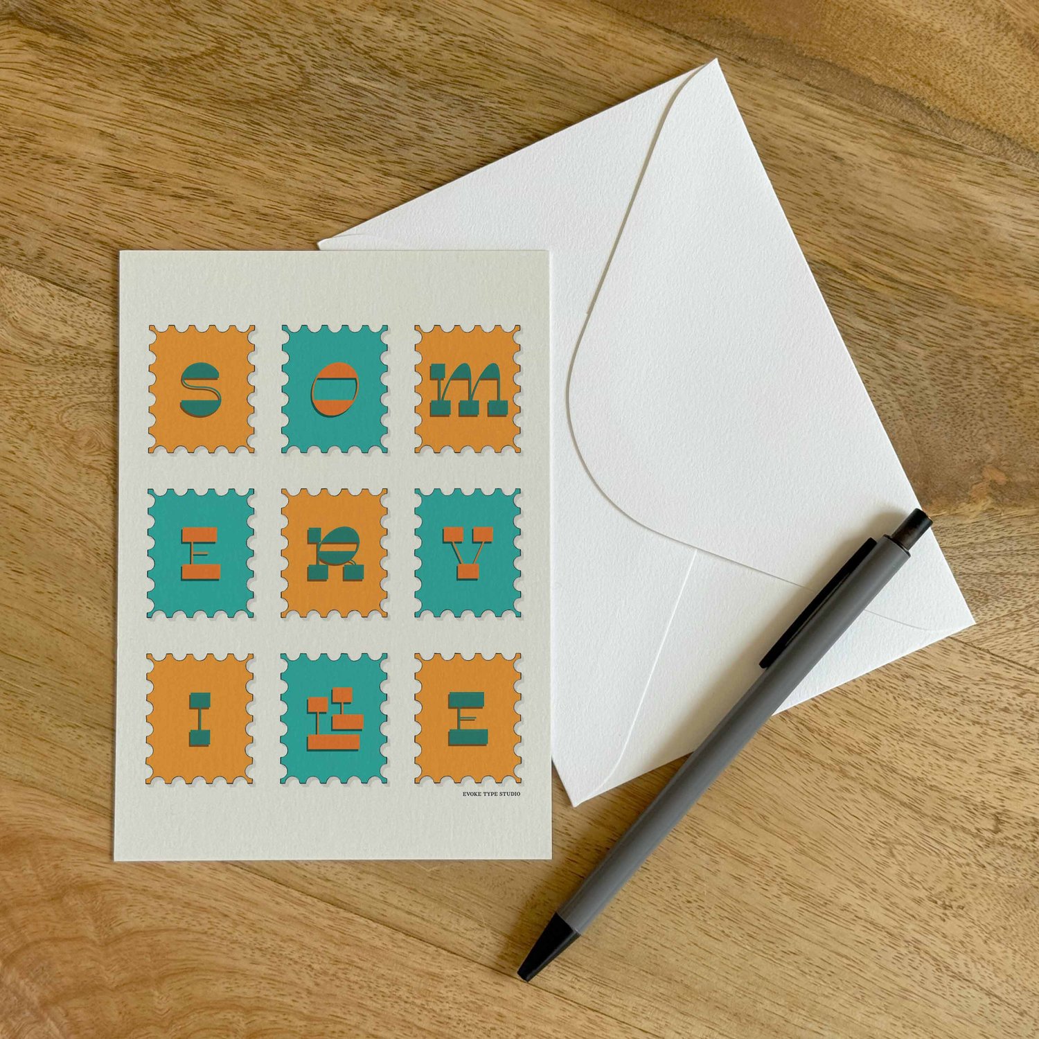 A colorful notecard sitting on a table with a white envelope and pen.