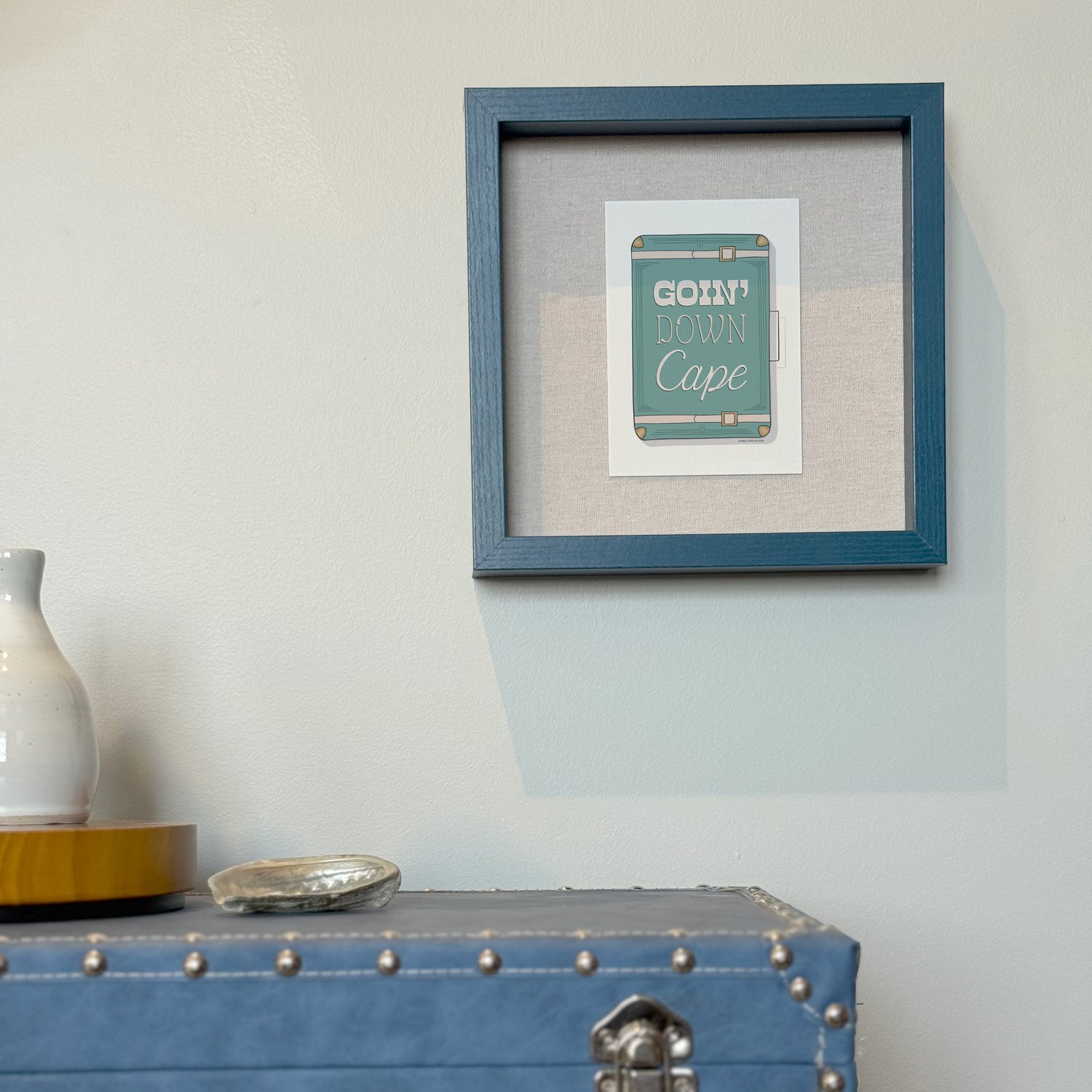 A framed notecard in a shadow box hung on the wall with decorative items placed nearby.