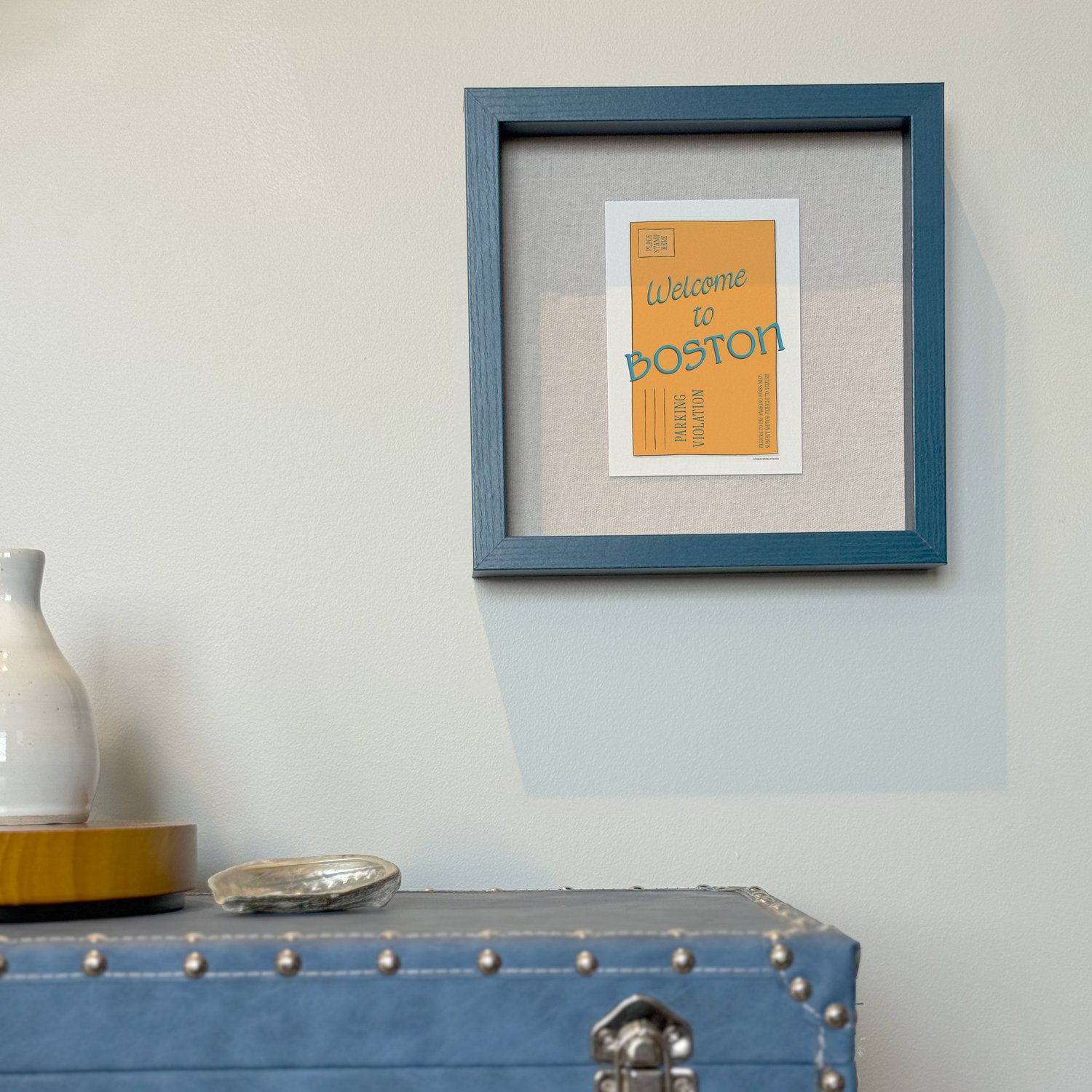 A framed notecard in a shadow box hung on the wall with decorative items placed nearby.