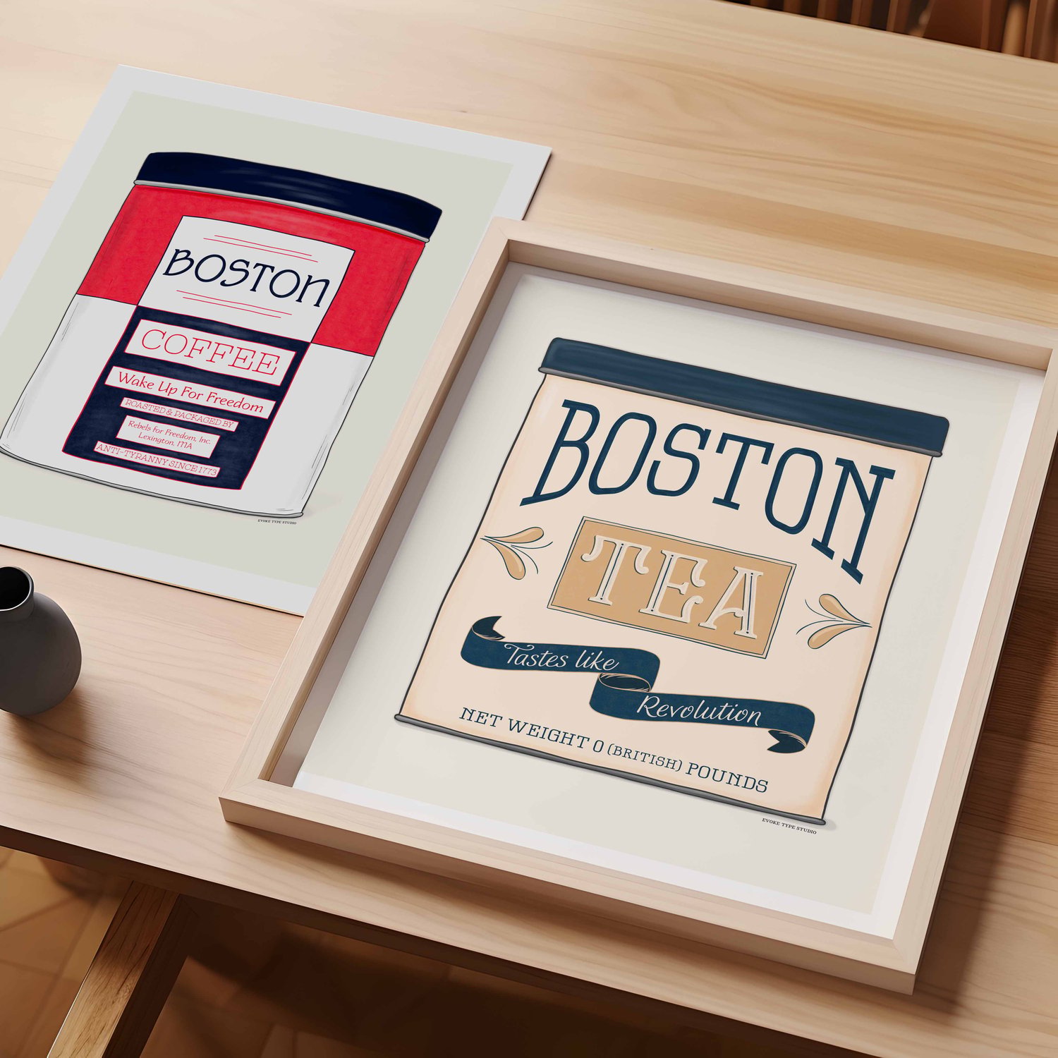 A table with an unframed artwork of a fake vintage Boston Coffee Tin and a framed artwork of a fake vintage Boston Tea Tin