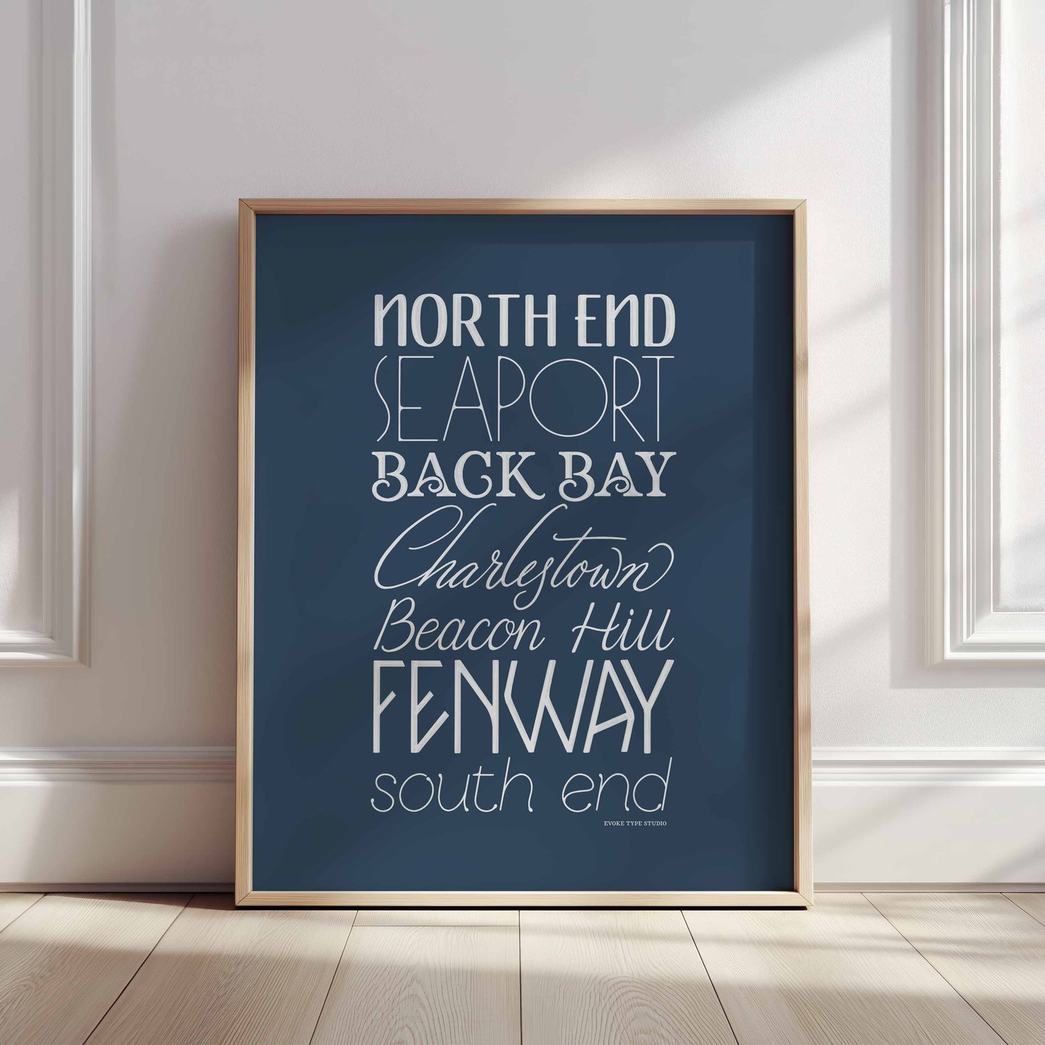A framed picture of Boston, Massachusetts neighborhoods drawn in various lettering styles. Artwork has a blue and white color scheme