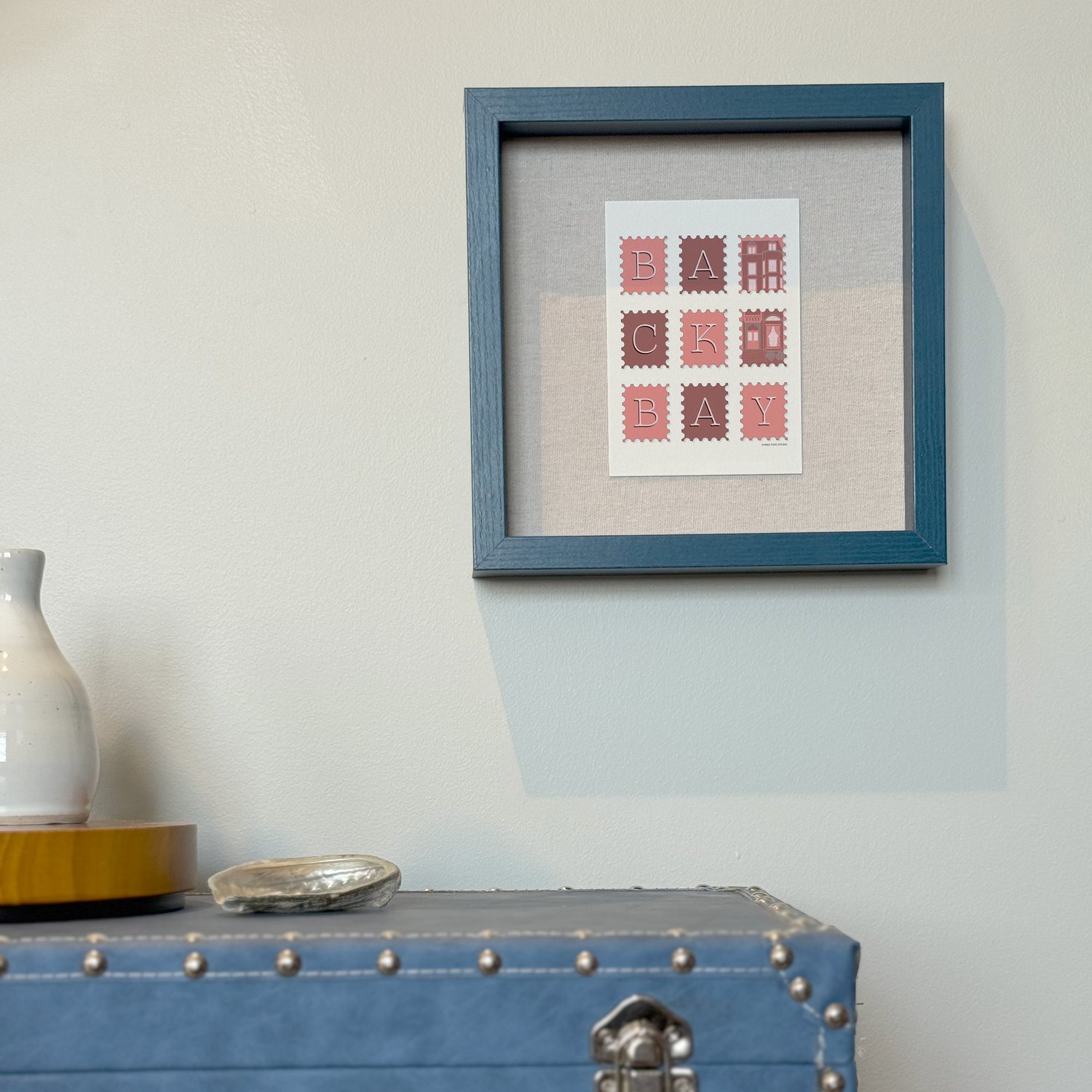 A framed notecard in a shadow box hung on the wall with decorative items placed nearby.