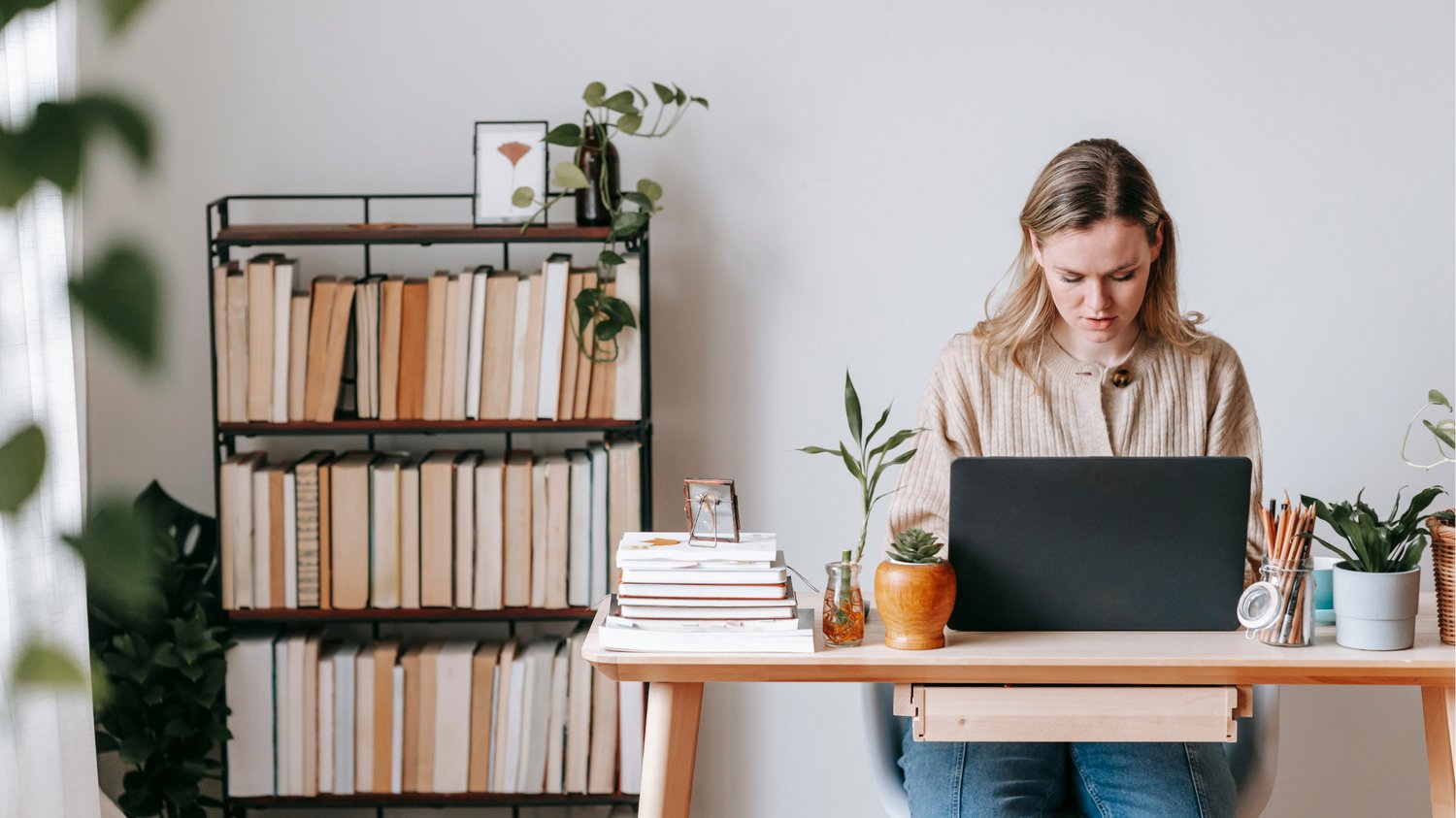 Health coach working at a laptop in a home office, surrounded by books and plants, representing email marketing strategy and content creation.