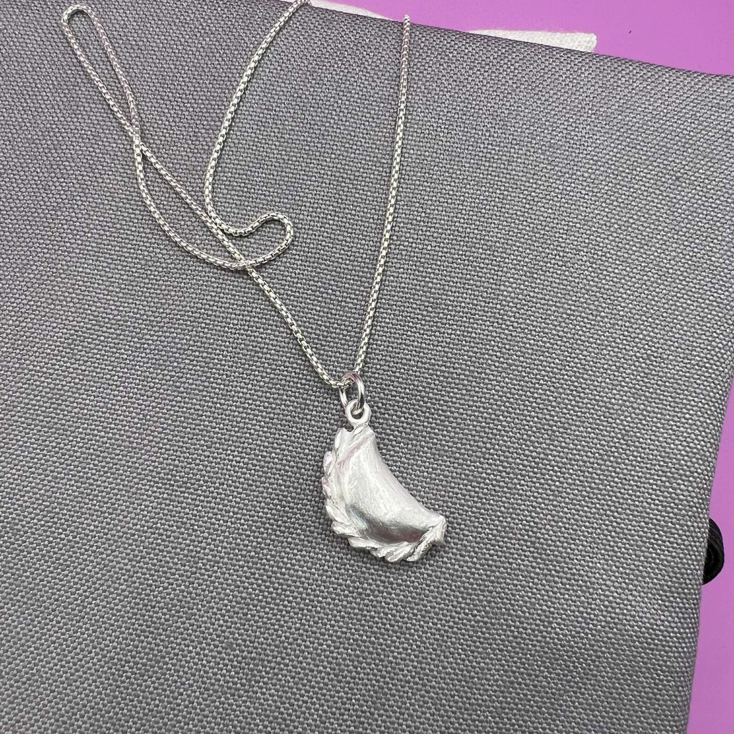 Silver curry puff pendant with chain, closer view
