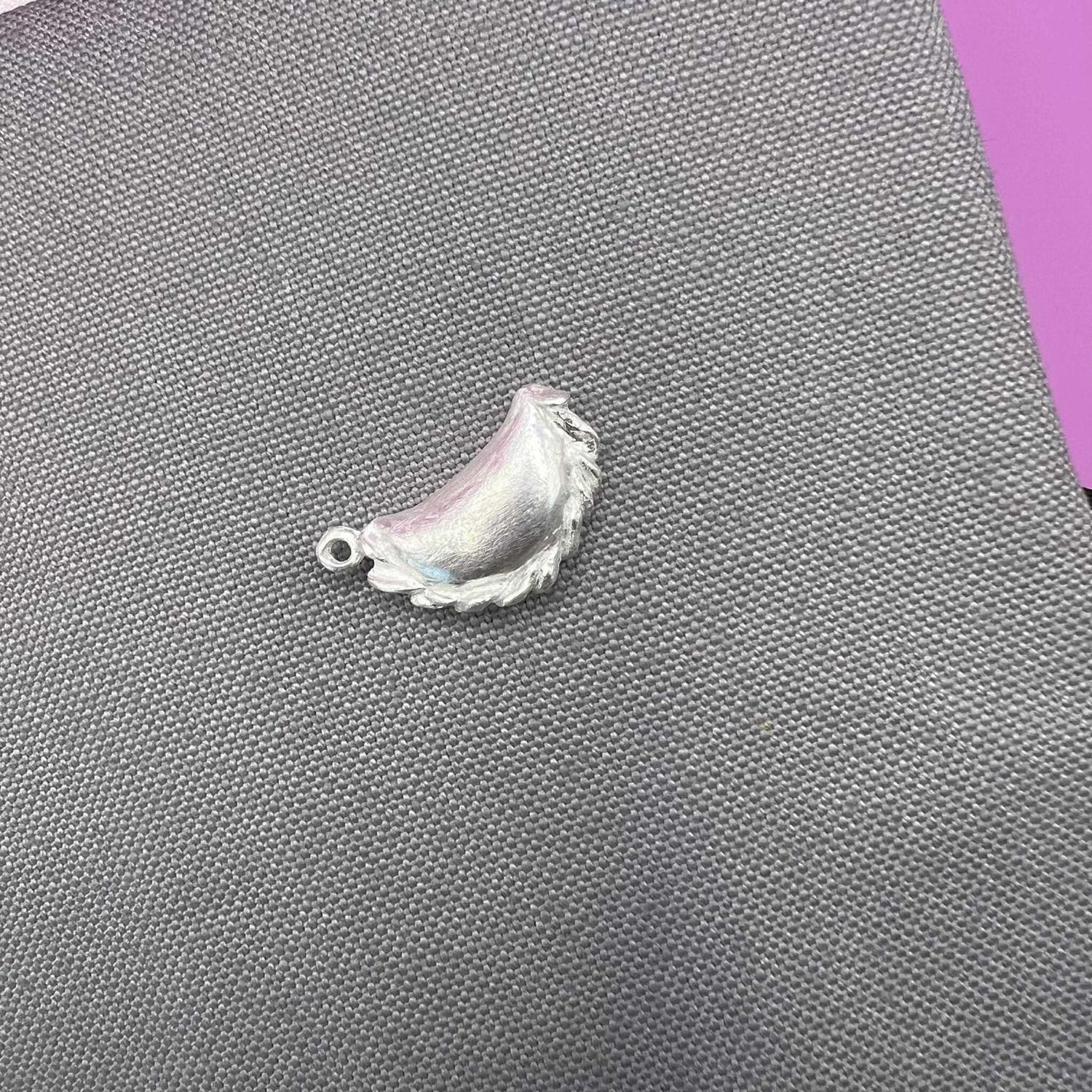 Silver curry puff pendant lying on the side on a light grey fabric
