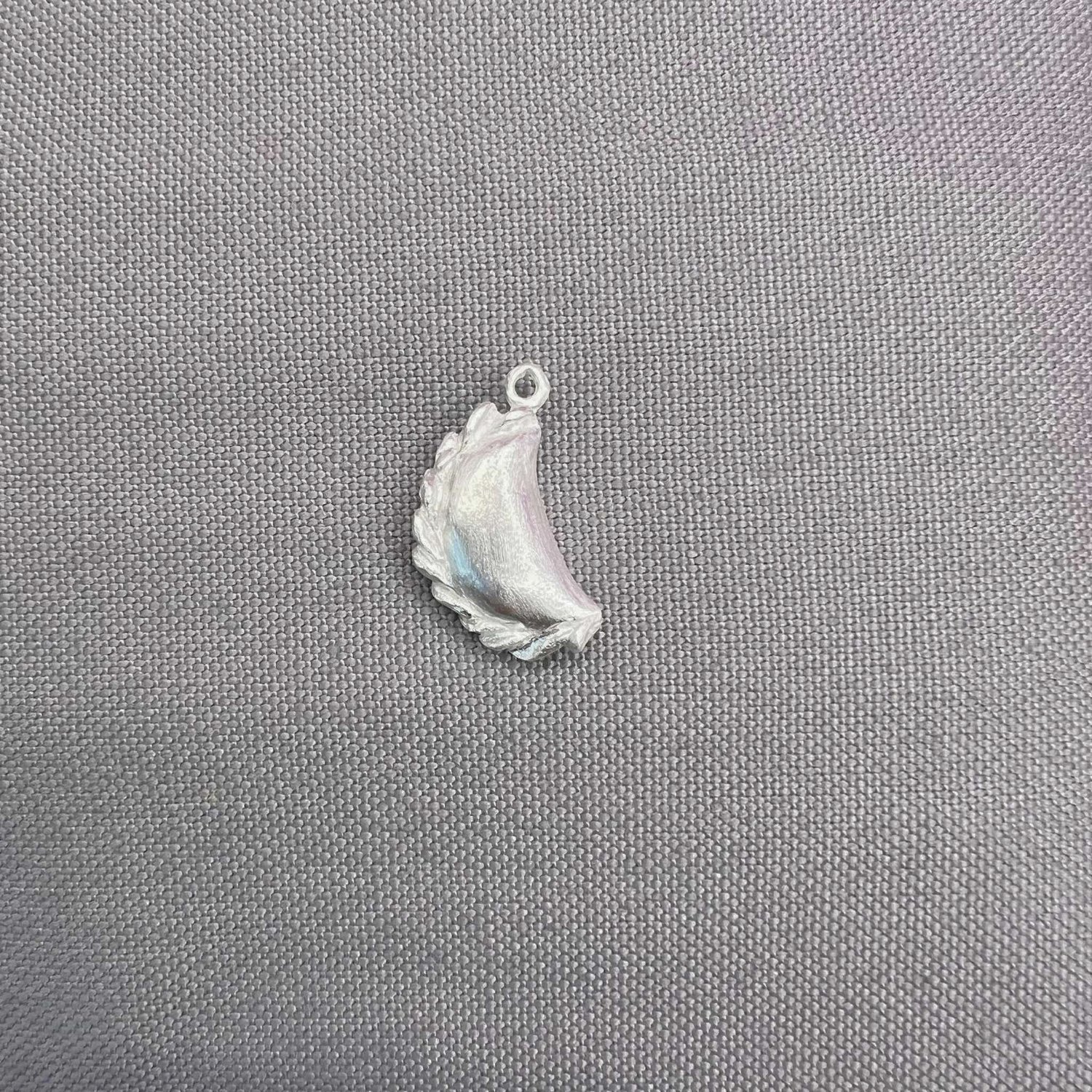 Silver curry puff pendant lying on a light grey fabric
