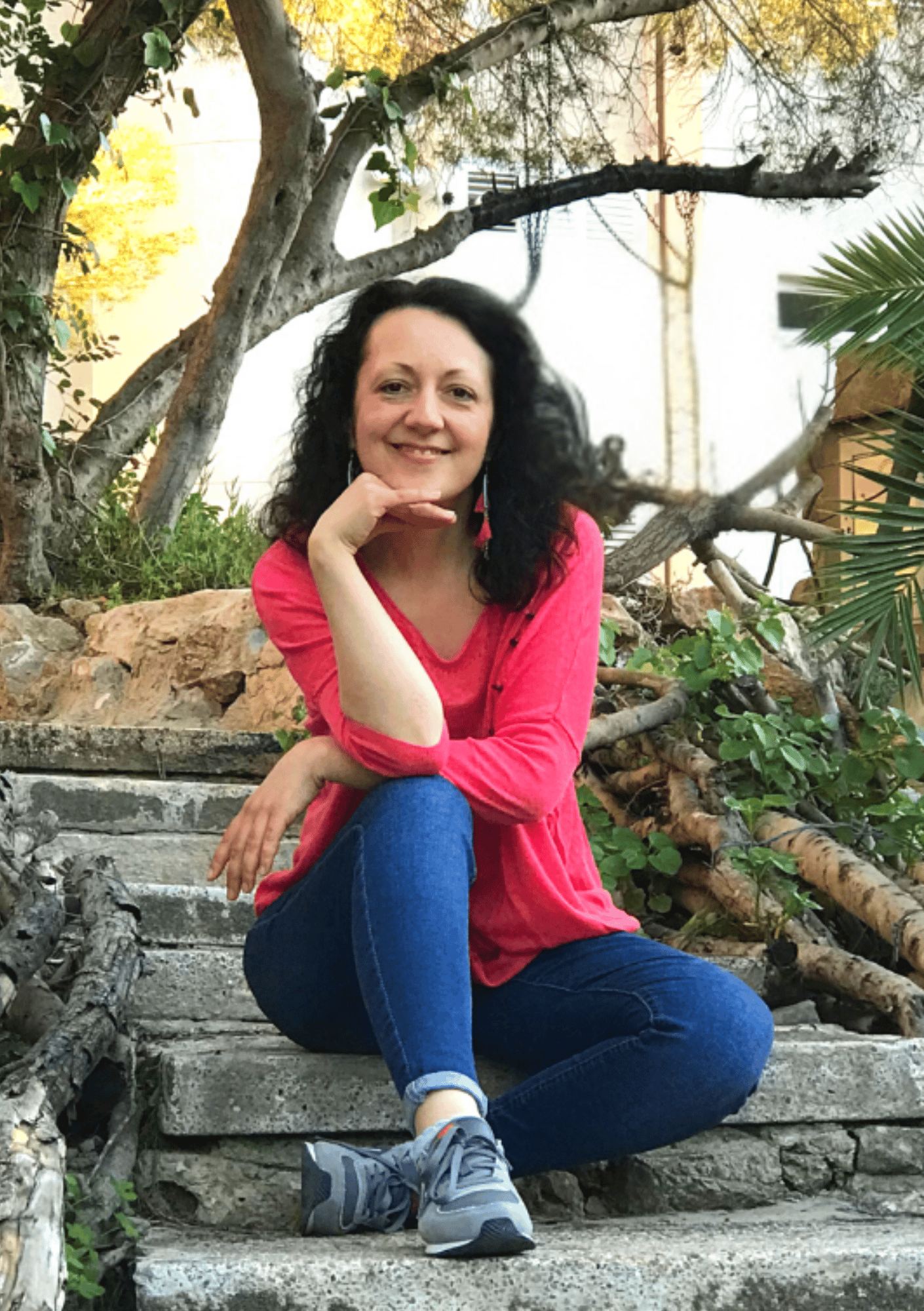 Isabel Bar sitting on stone steps in nature wearing a bright pink top and jeans, smiling — About page on iamisabelbar.com