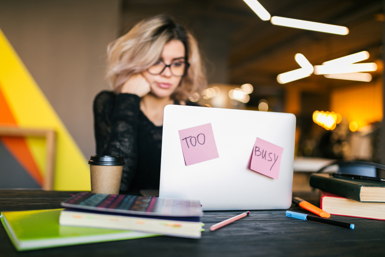Bureau avec ordinateur portable et post-it 'TOO BUSY', illustrant le point de départ d'une surcharge avant la conception d'une journée de travail idéale et personnalisée.