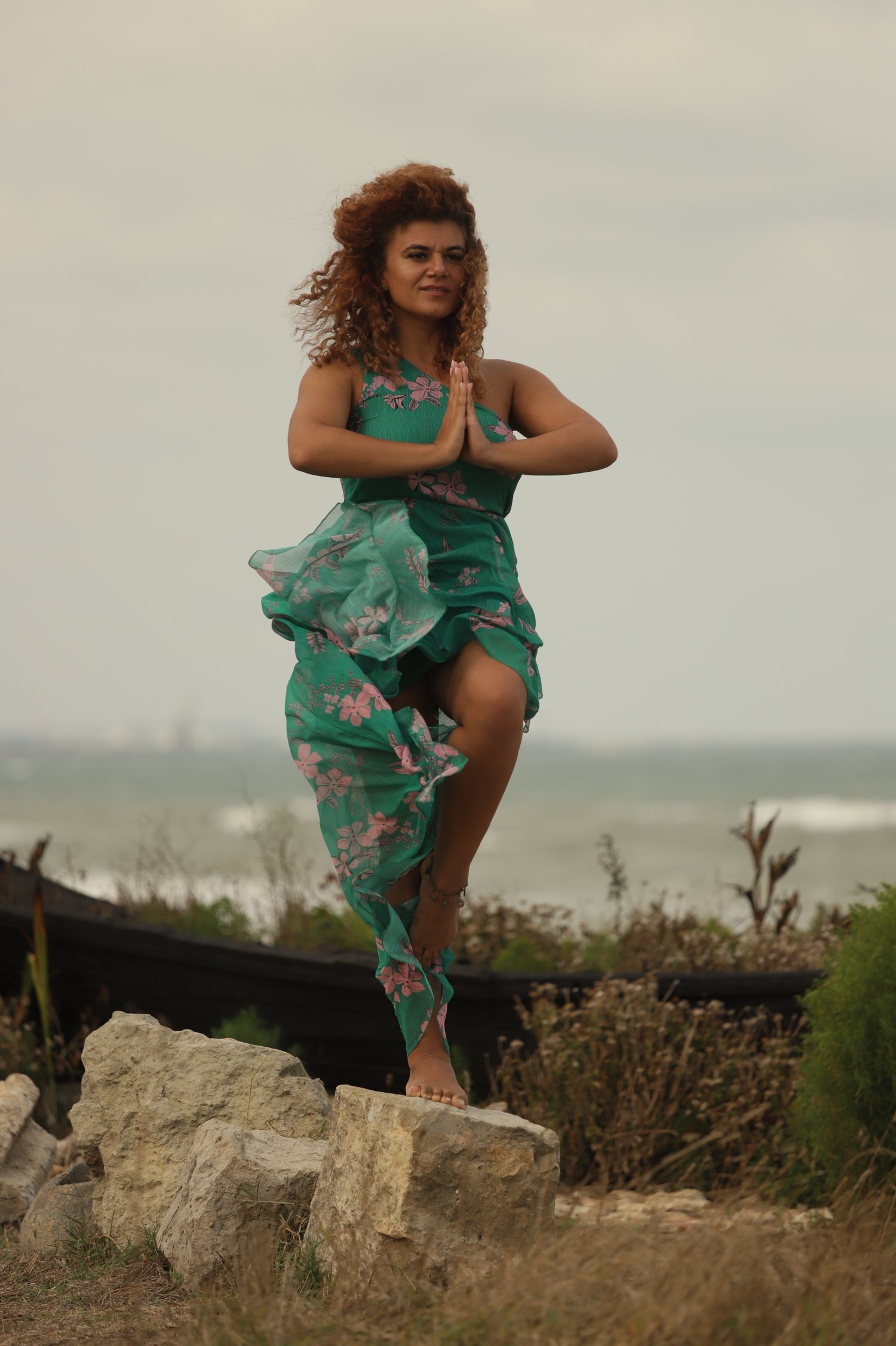 Femeie în postură de yoga Garudasana în natură, într-o rochie verde cu flori – simbol al echilibrului interior și al prezenței, alchimia vietii