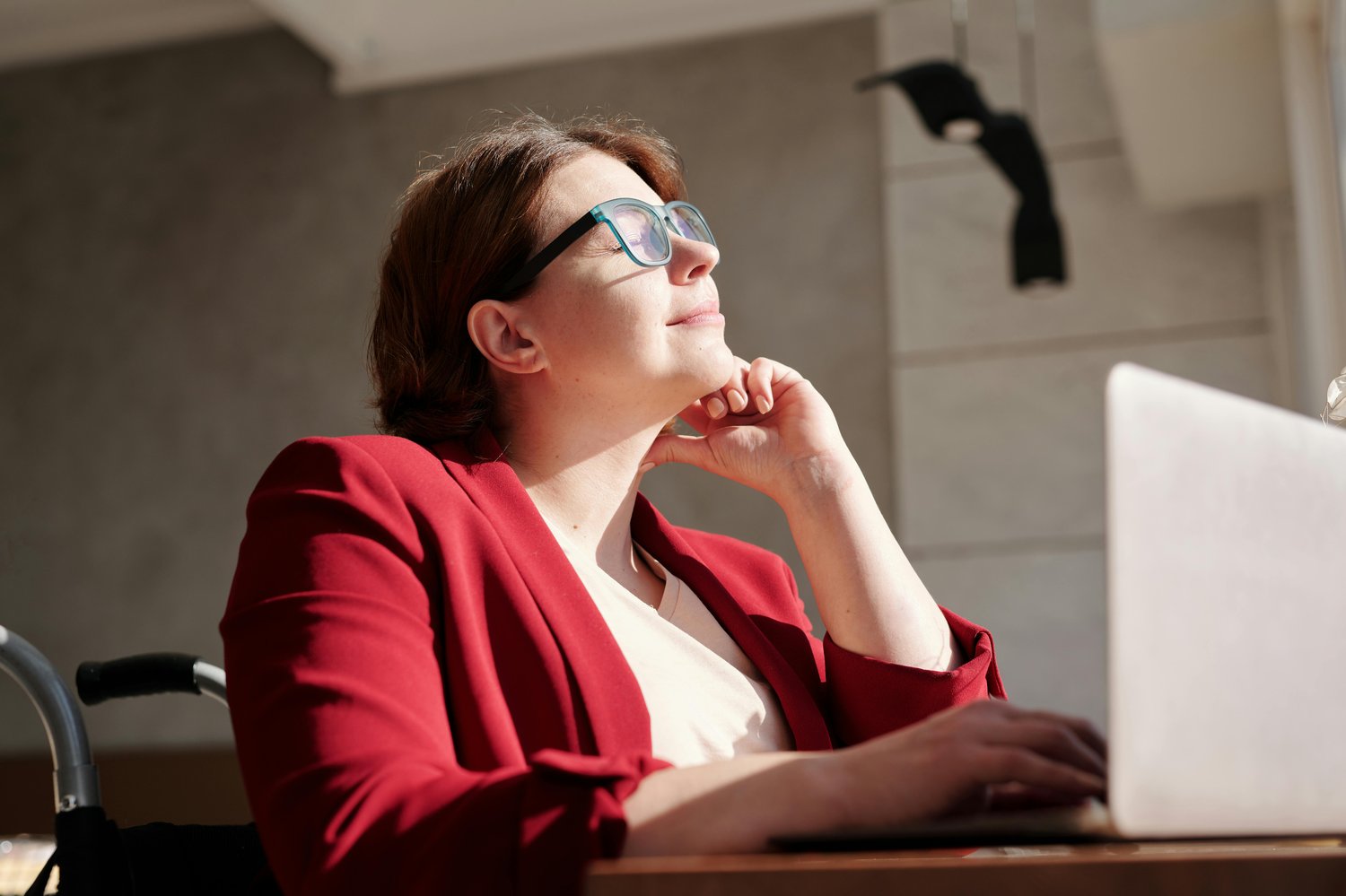 a young woman basking in the window sunlight as she works at her laptop sitting in her wheelchair