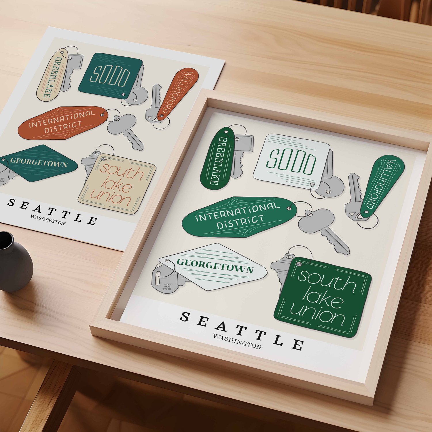 A table with an unframed artwork of Seattle key fob art and a framed artwork of Seattle key fob art